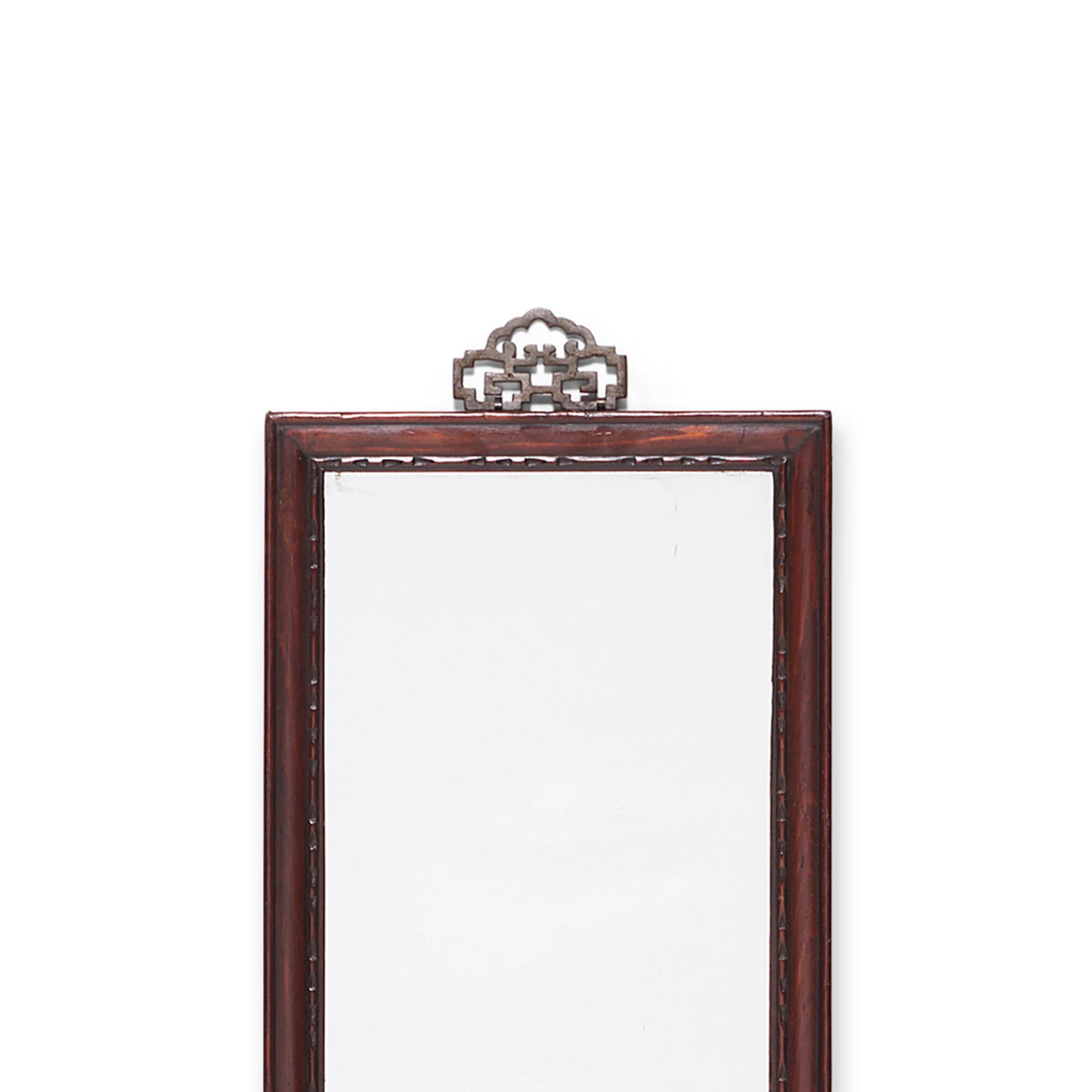 This early 20th century mirror is crafted of hand carved pine and once hung on the wall of a Qing-dynasty home, perhaps in a ladies sleeping quarters. Subtle notches pattern the frame's finely beaded edges and brass hardware adorns the top, formed
