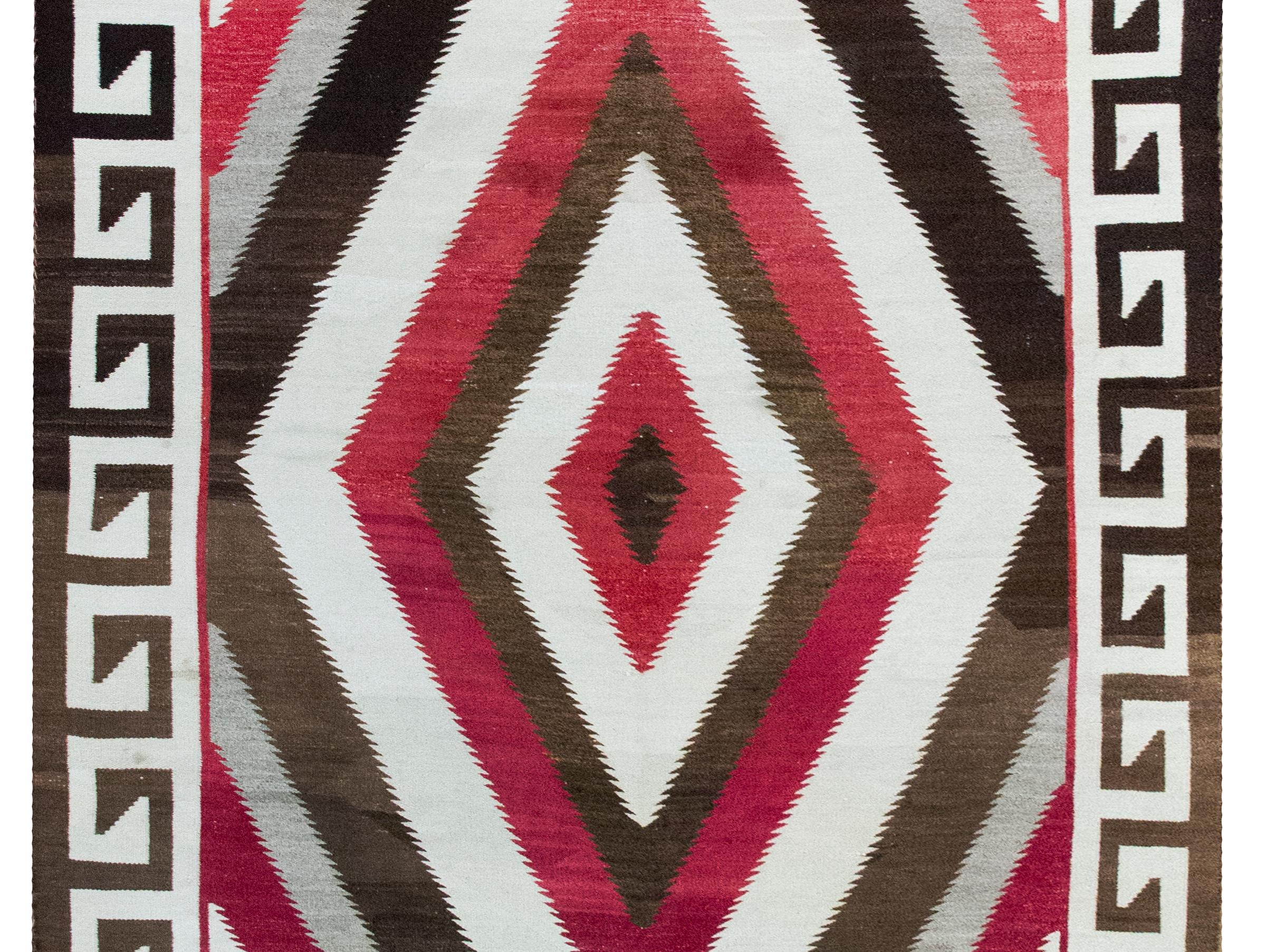 Dieser außerordentlich seltene großformatige Navajo-Teppich, der um 1900 gewebt wurde, ist ein beeindruckendes Beispiel indigener Kunstfertigkeit in großem Maßstab. In der Mitte befindet sich ein Medaillon aus naturbraunen Diamanten, von dem eine