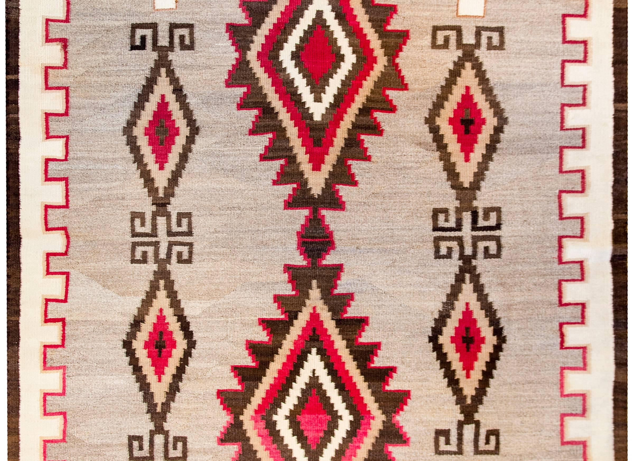 A gorgeous early 20th century Navajo rug with a bold pattern containing multiple large-scale diamonds amidst a field of abrash natural grey and cream colored wool. The border is wide with a thin red zigzag stripe and cream colored outer border.
 