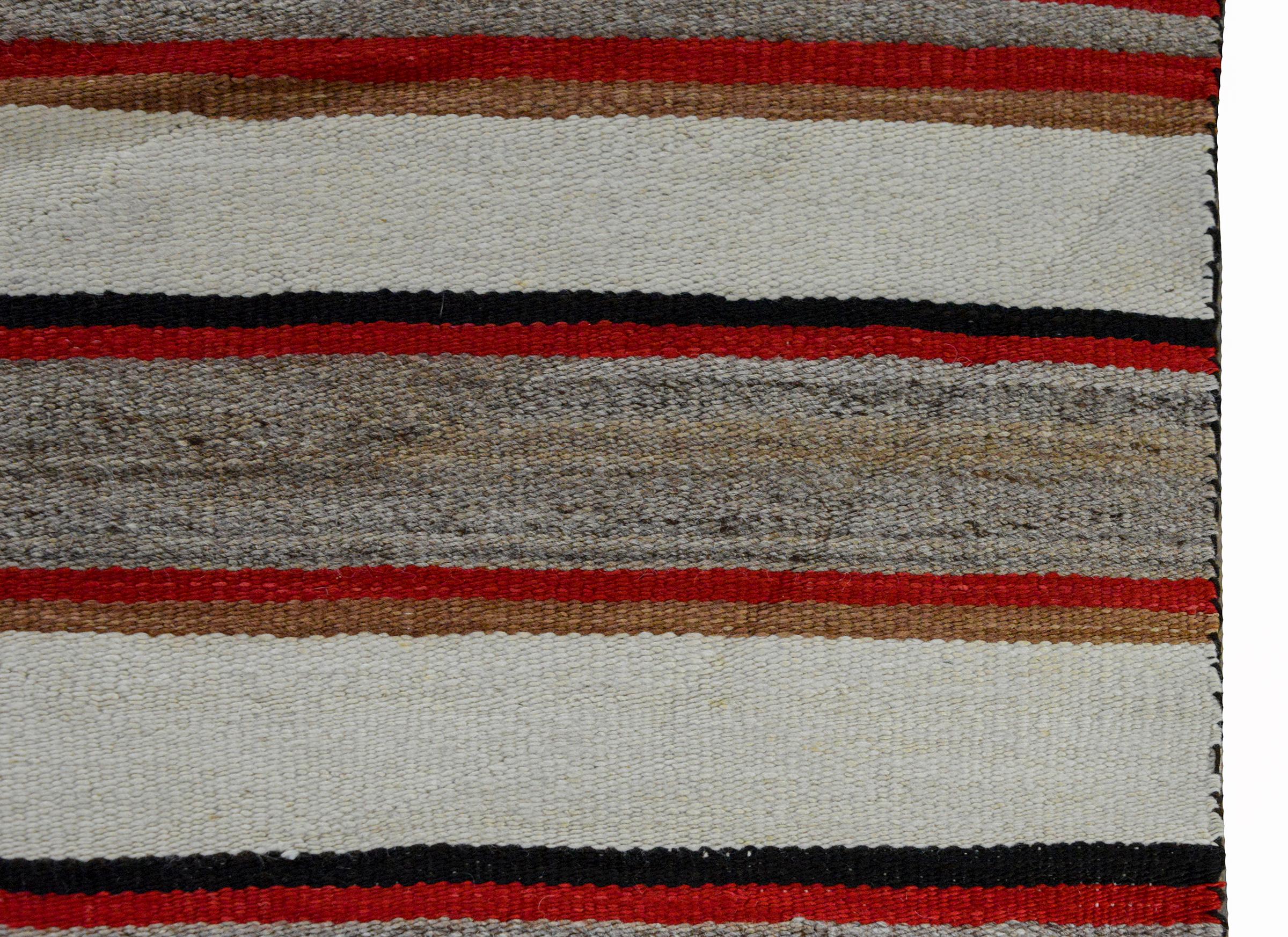 An early 20th century Native American Navajo rug with red, gray, black, tan, and white stripes in the center, and geometric zigzags and diamonds at opposite ends.