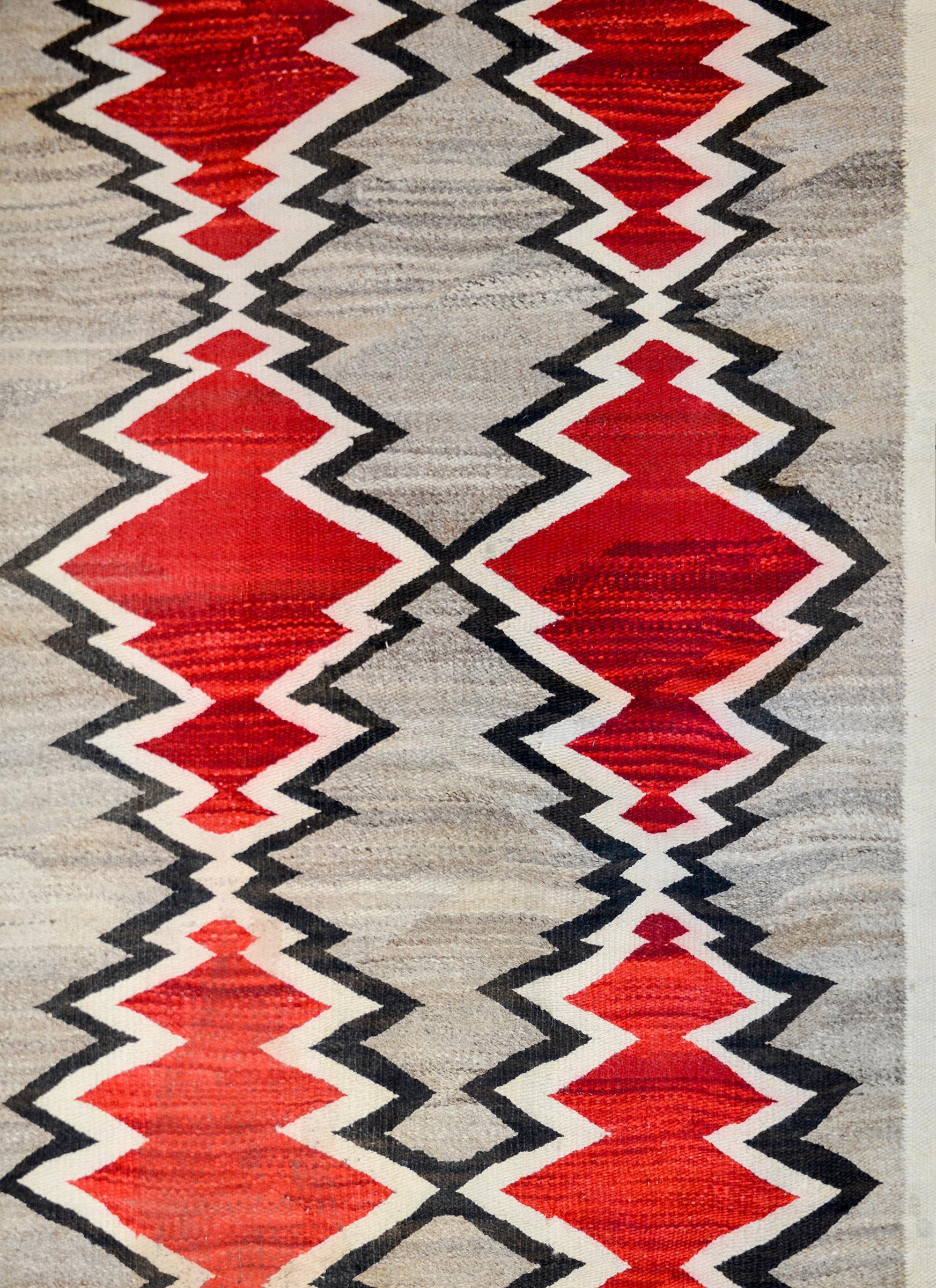 A gorgeous early 20th century Navajo rug with a repeated large scale abrash crimson diamond pattern on an abrash grey ground surrounded by a simple black and white striped border.