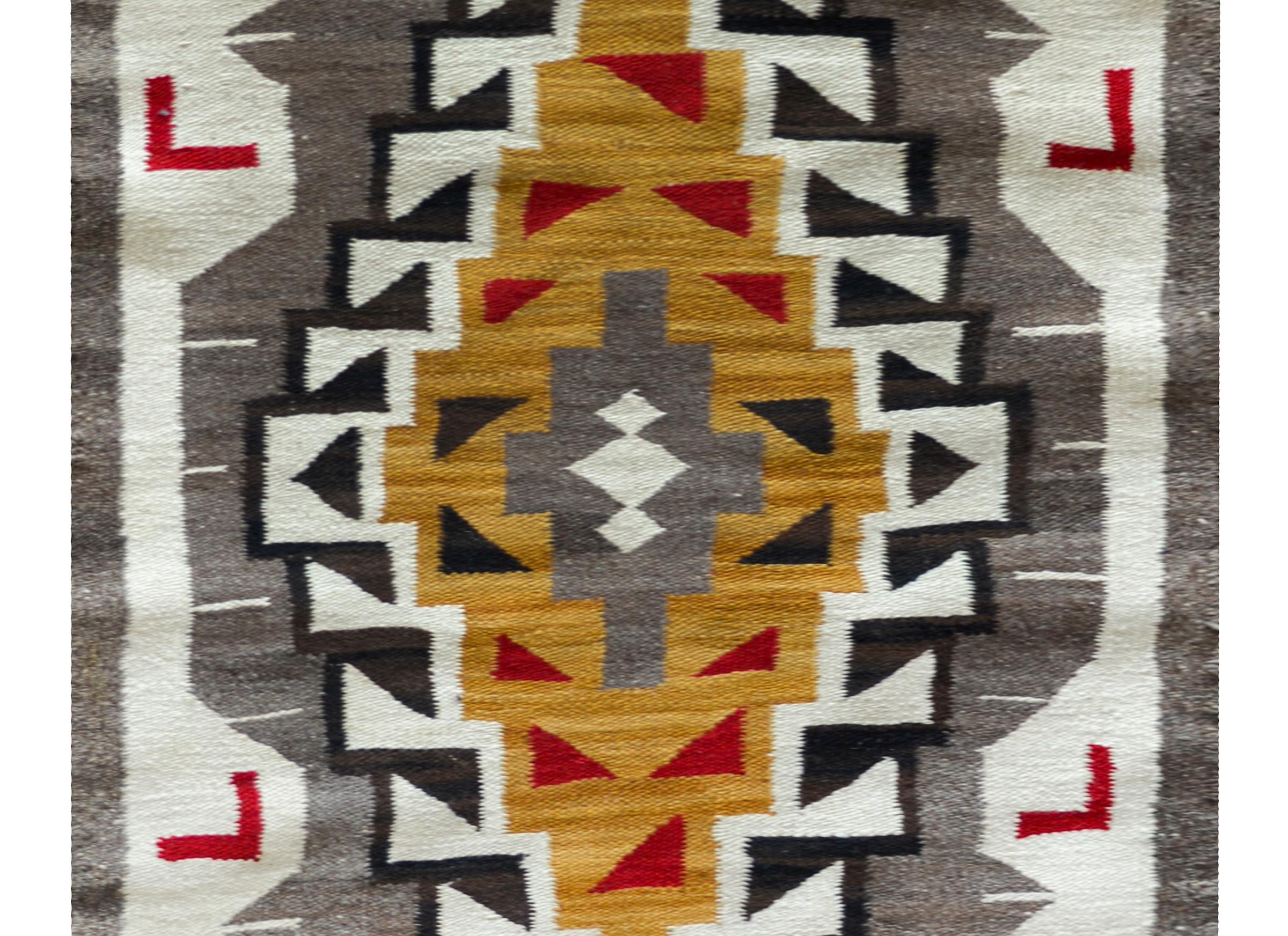 An early 20th century Navajo rug with a wonderful geometric pattern including a large central diamond medallion floating over a gray field and flanked by pairs of orange wings at each end. The border is playful with several red geometric patterns