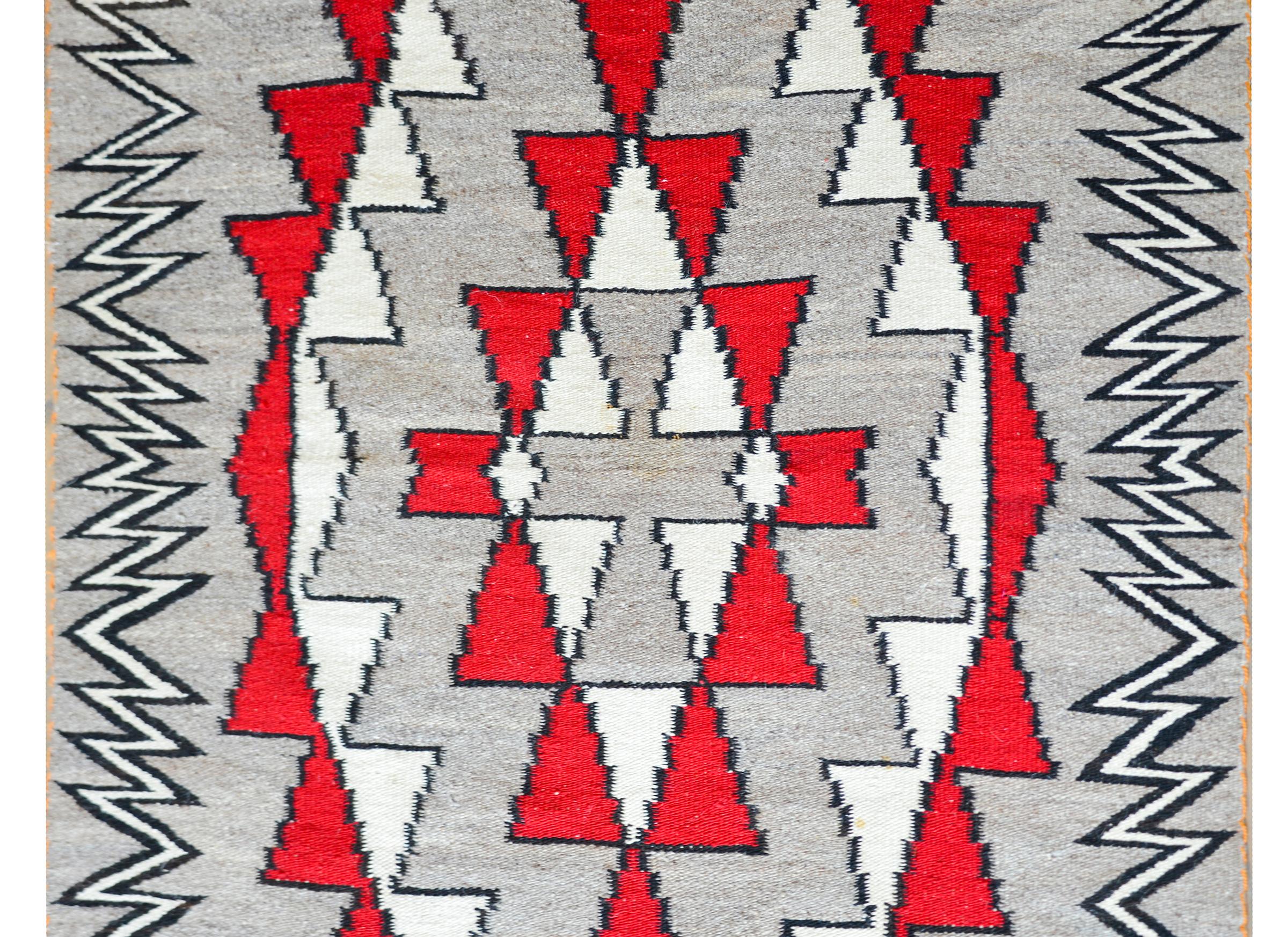 A striking early 20th century Native North American Navajo Rug with a bold geometric diamond pattern woven in crimson and white wool against a gray background, and with a fantastic black and white zigzag patterned border.