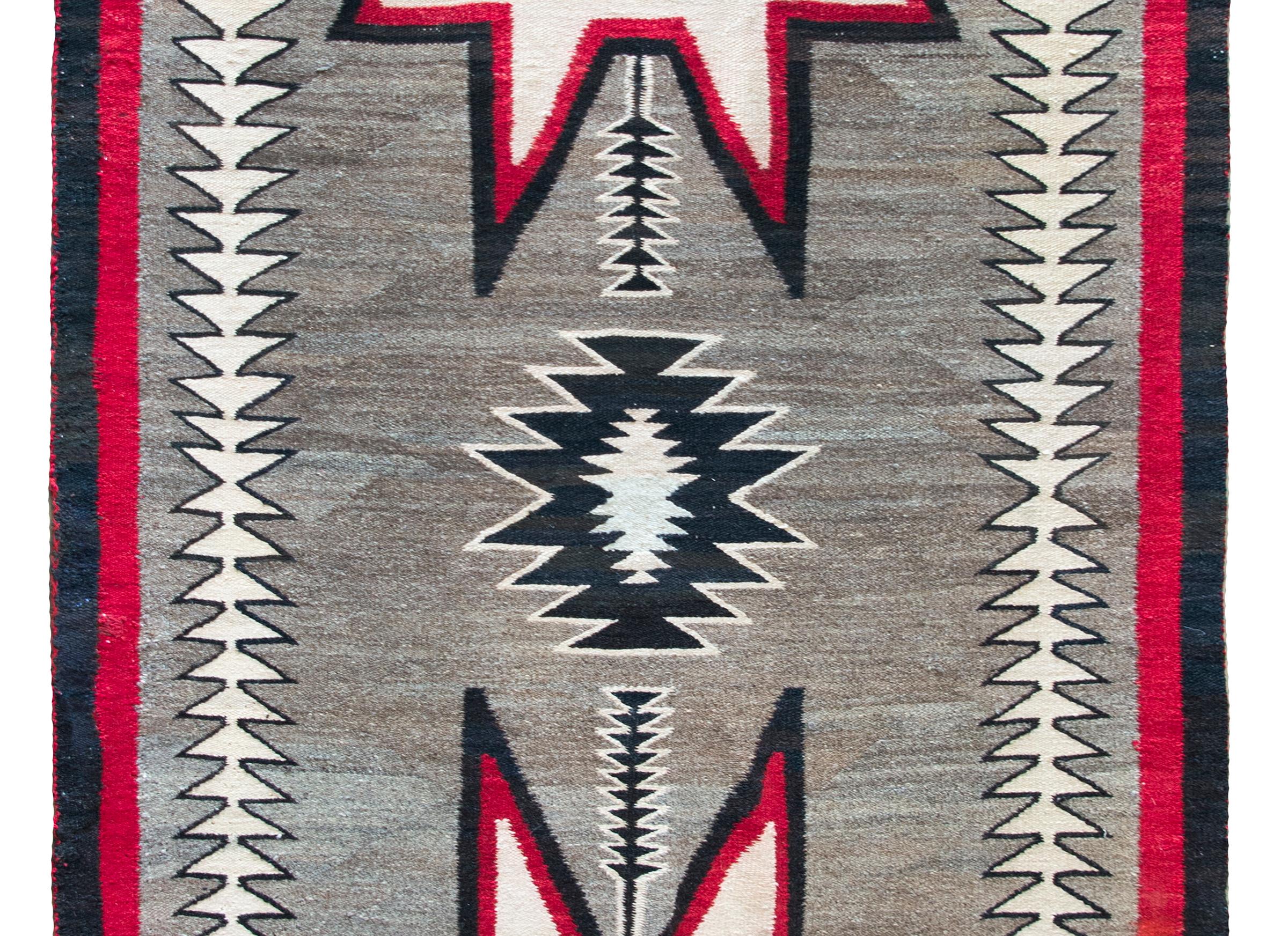 A stunning early 20th century Native American Navajo flatweave rug with two incredible large star-shaped medallions flanking a central smaller black medallion set against a natural abrash gray wool ground, and surrounded by a simple border with