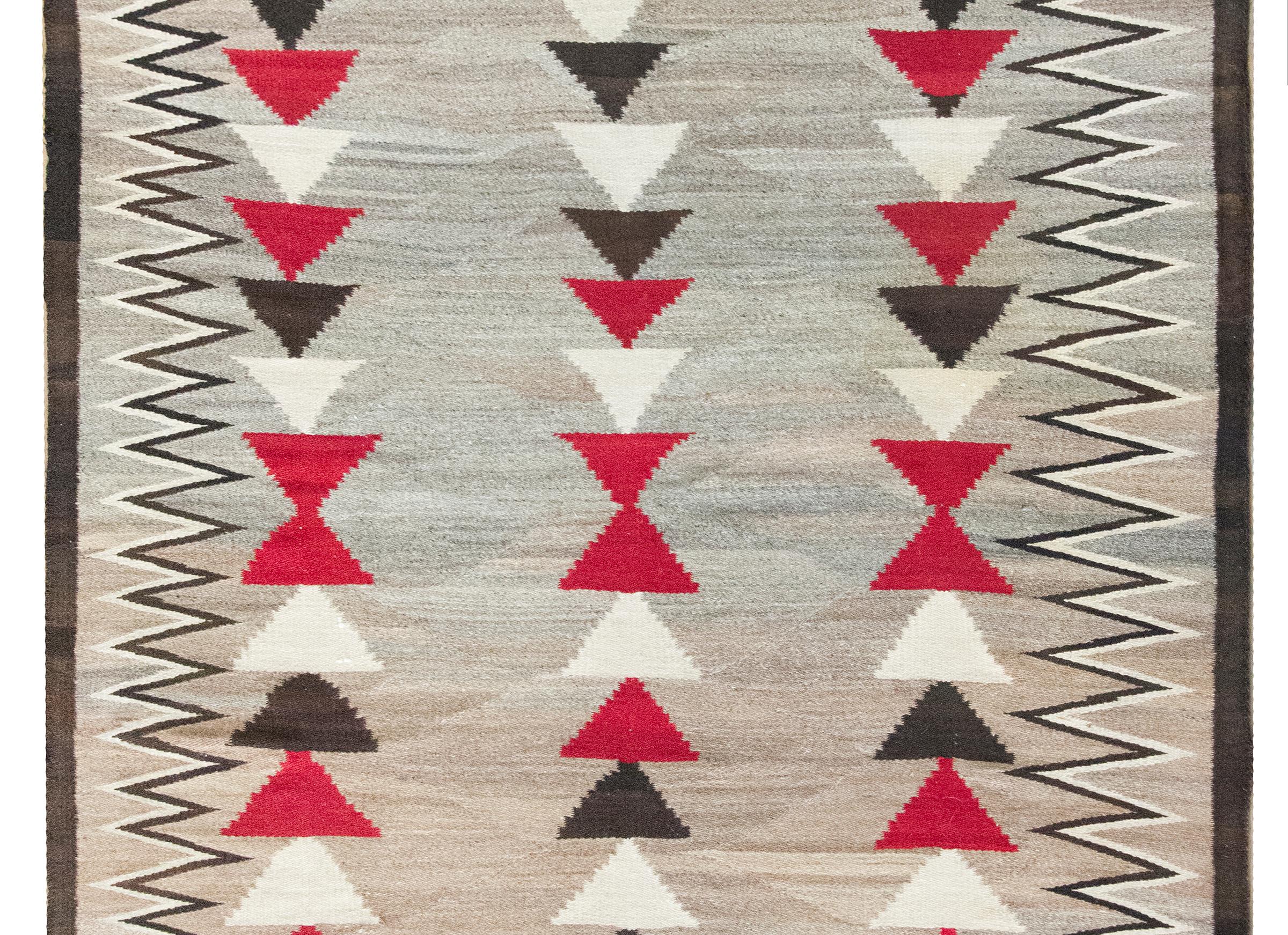 This early 20th century Navajo rug is a striking example of Indigenous textile artistry—woven with natural wool in a bold, graphic composition that feels at once timeless and modern. The central field, composed of soft abrash grays and browns, is