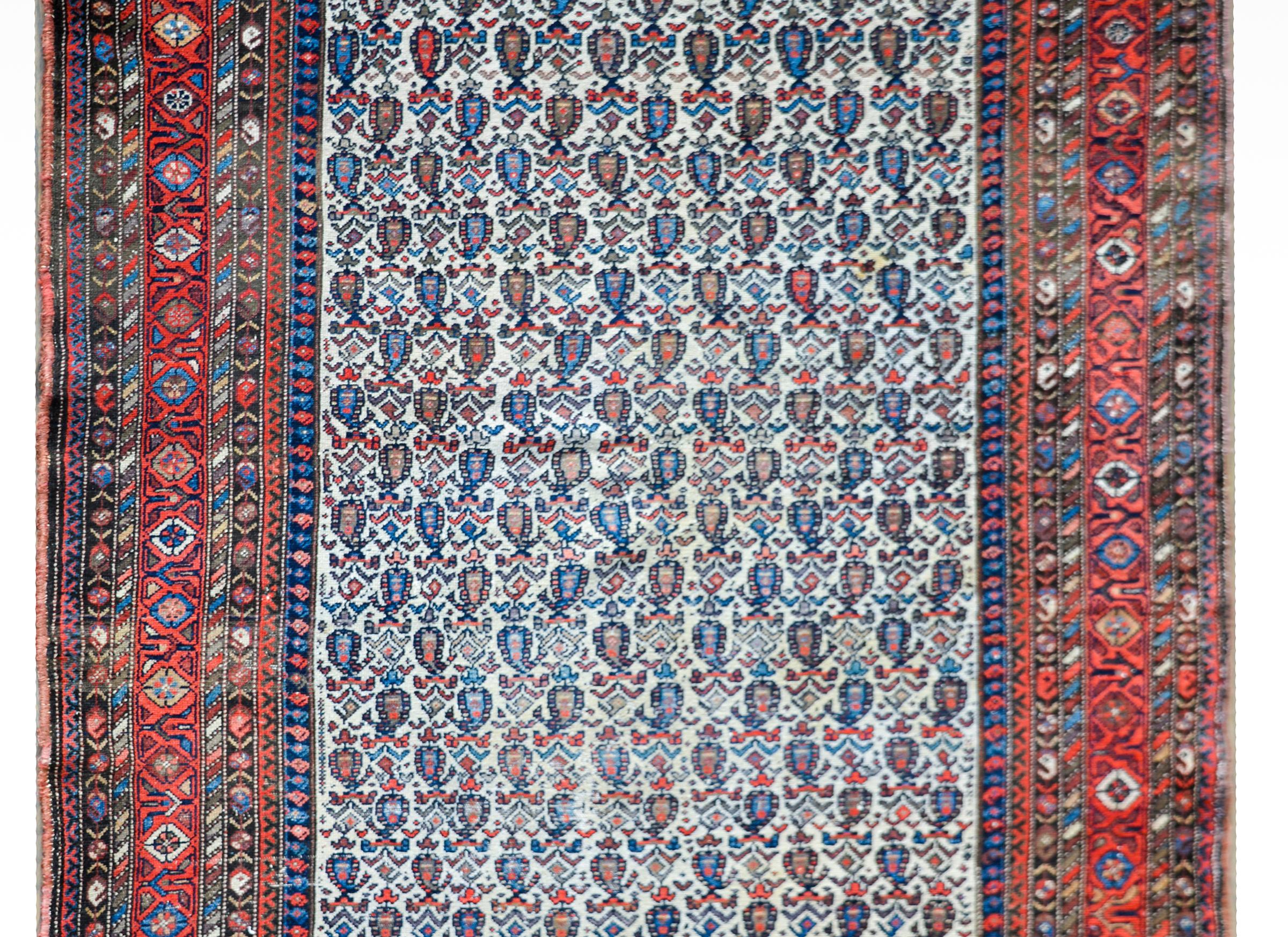 A wonderful early 20th century Persian Nehband rug with an all-over paisley and stylized floral pattern woven in myriad colors including crimson, indigo, gold and brown, against a cream colored background. The border is wide with multiple petite
