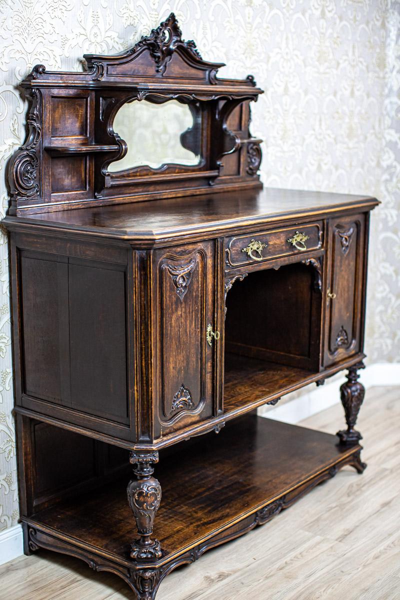 We present you a solid oak sideboard from first quarter of the 20th century.
This piece of furniture is composed of a platform on legs, with a two-leaf base placed on it and a wide niche in the middle.
The upper section is in the form of an add-on