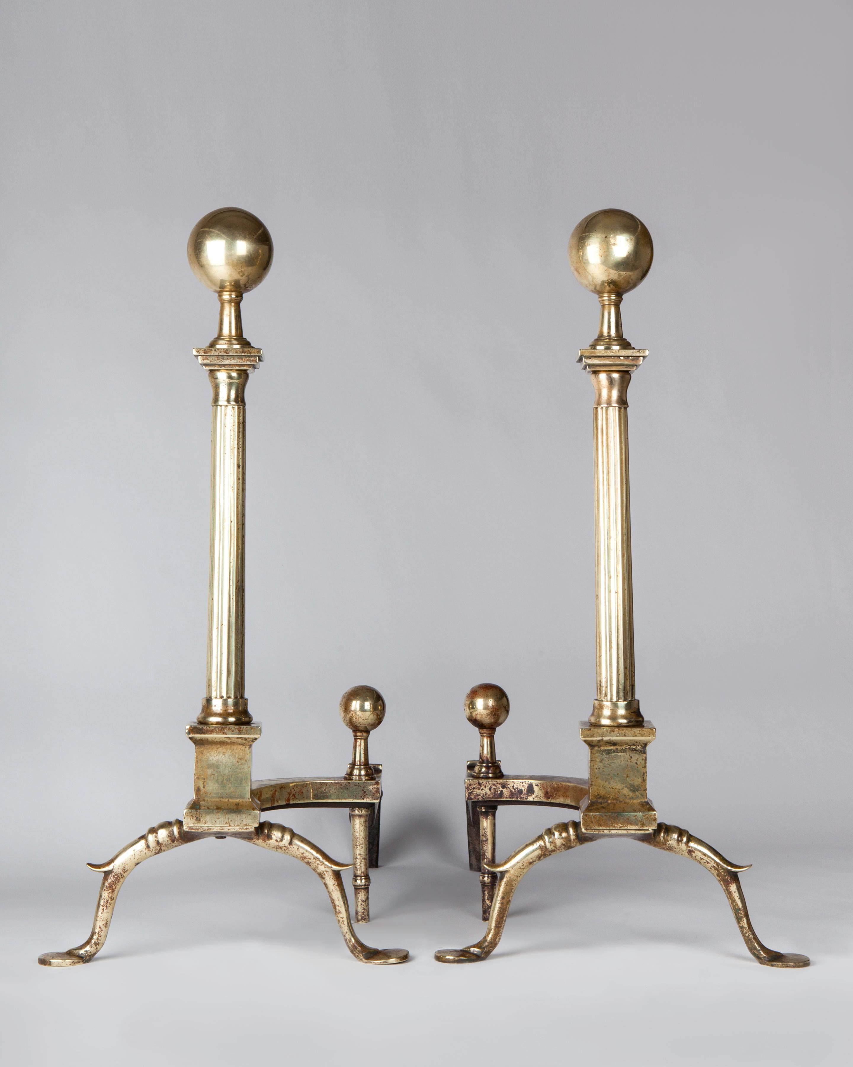 AFP0632

A pair of antique brass andirons of superb quality, having fluted column shafts with ball finials set on rectangular plinths and cusped legs. The offset backs are accented with small brass ball finials and drop legs. In an aged polished