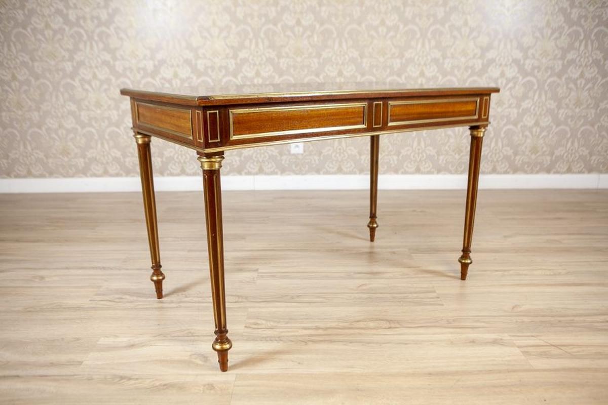 Vintage Neoclassical Writing Desk Inlaid With Brass, 1950s

An exquisite neoclassical-style writing desk crafted in the early 1950s exemplifies timeless elegance and refined craftsmanship. The piece features a rectangular top supported by four tall,
