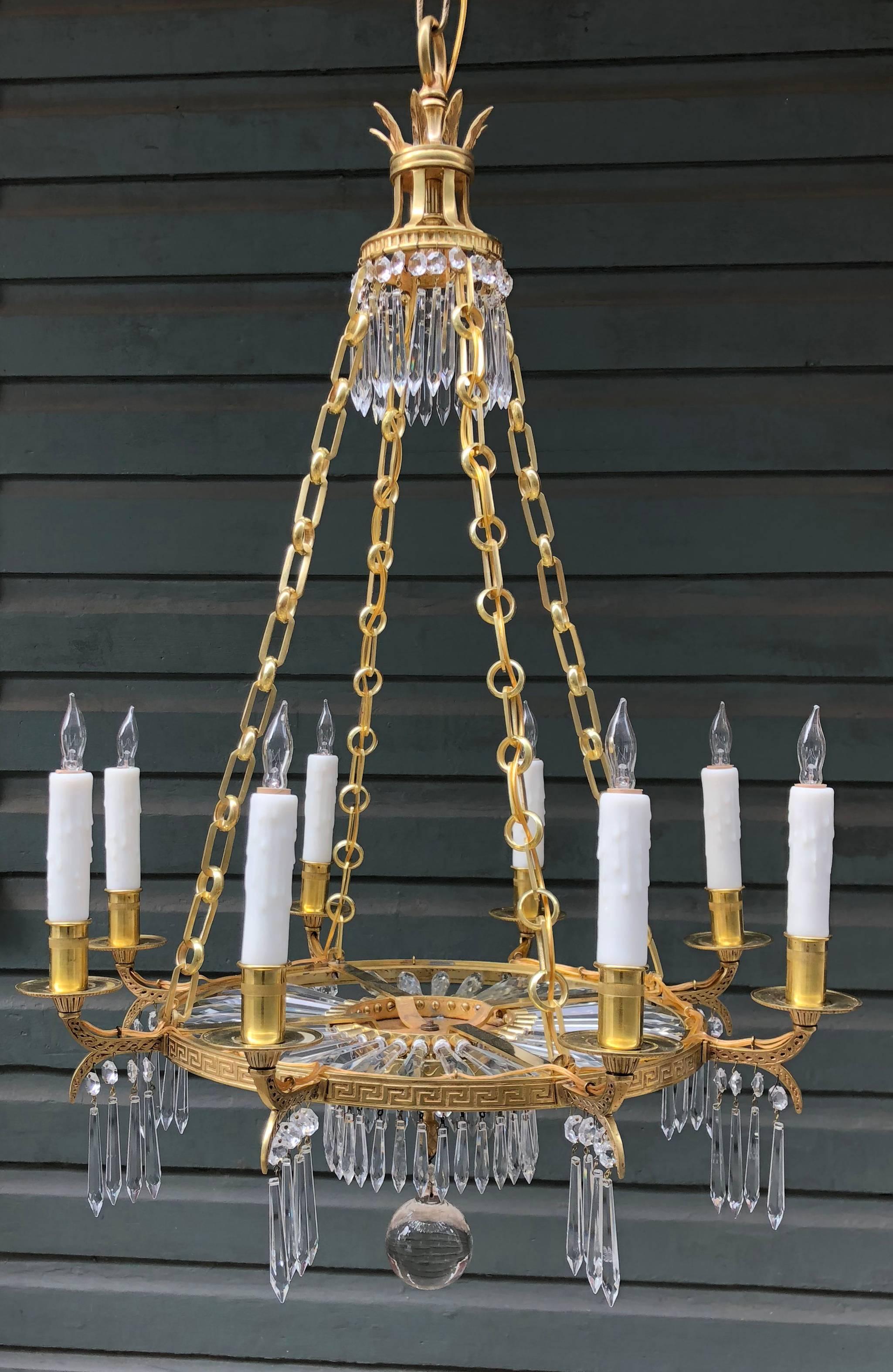 This early 20th century New York chandelier is attributed to Caldwell. This doré bronze chandelier is accented with a Greek key and eight stylized palm frond arms with Regency bobeches. Wonderful crystal sunburst bottom.