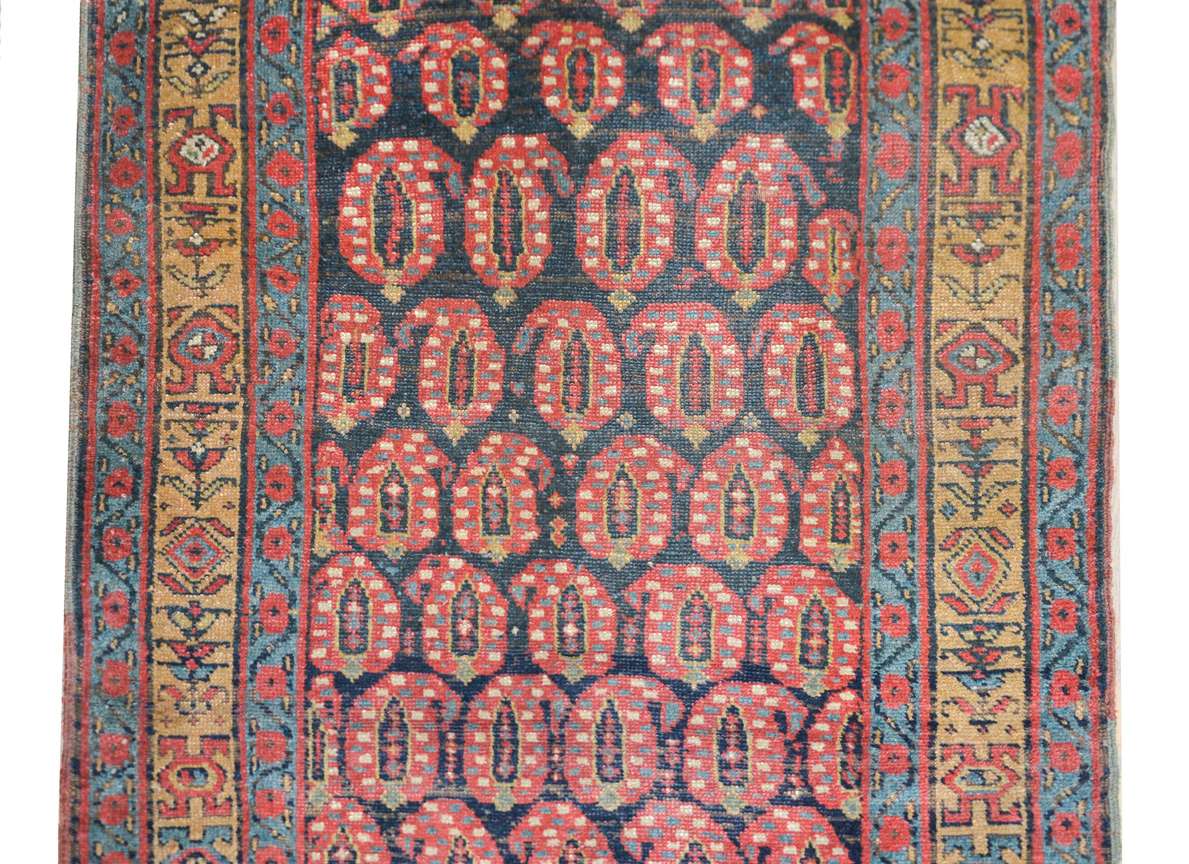 A wonderful early 20th century N.W. Persian runner with an all-over paisley pattern woven in crimson, gold, light indigo, and white and all set against a dark indigo background. The border is sweet with a central stylized floral patterned stripe