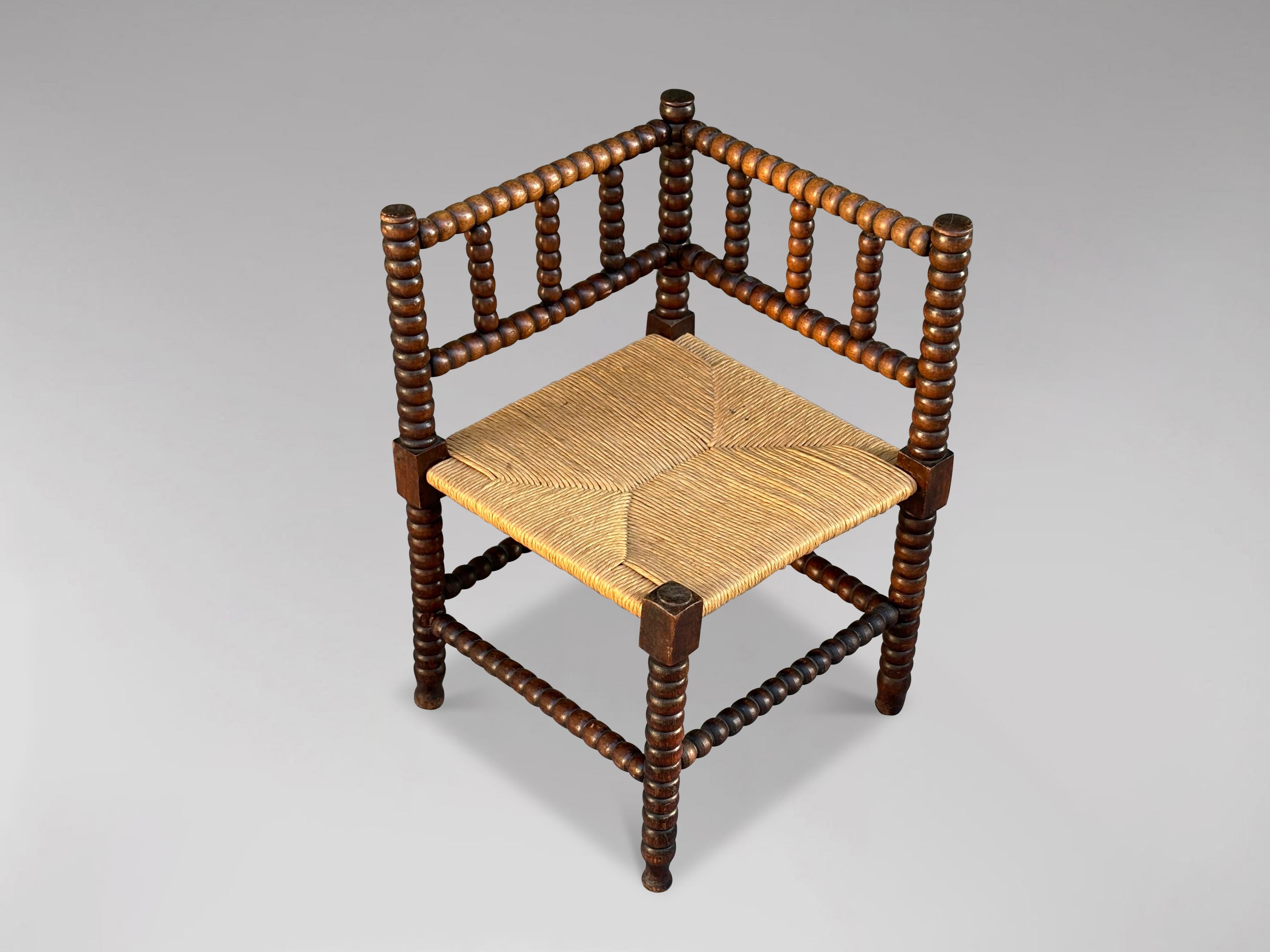 Charmante chaise d'angle en bois au fuseau du début du 20e siècle. Il se compose de cadres en chêne magnifiquement tournés et de sièges en jonc rayé d'origine. Provenant du South Antiques, il est en très bon état de conservation. Cette chaise