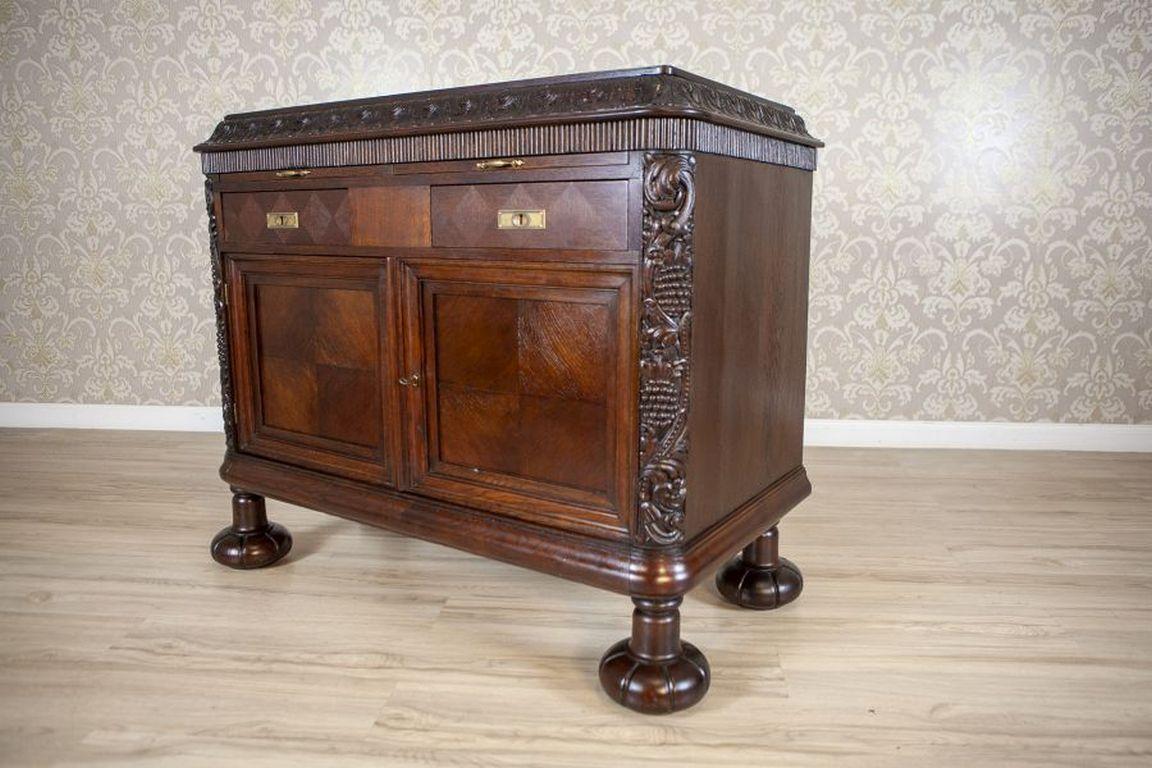 Early-20th Century Oak Commode in Brown With Drawers

An oak commode, dated to the Interwar Period, featuring two drawers and shelves located behind lockable doors. The piece is adorned with floral motifs and finished with elliptical legs. The