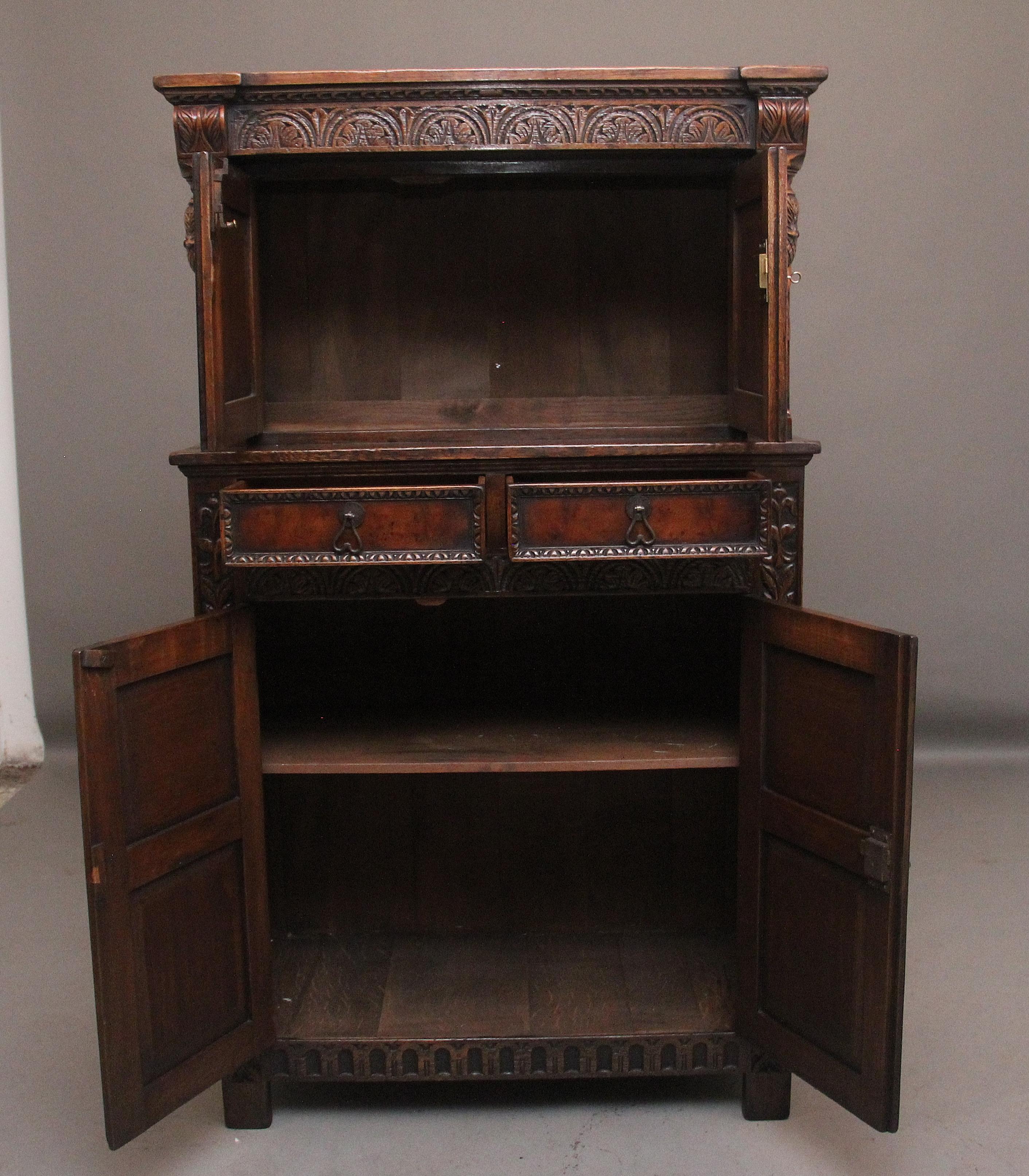Credenza di corte in rovere intagliato dei primi del Novecento, con la parte superiore composta da un fregio intagliato con ghiande pendenti ai lati, sopra due ante di credenza con pannelli ovali intagliati che si aprono per rivelare un ampio vano,