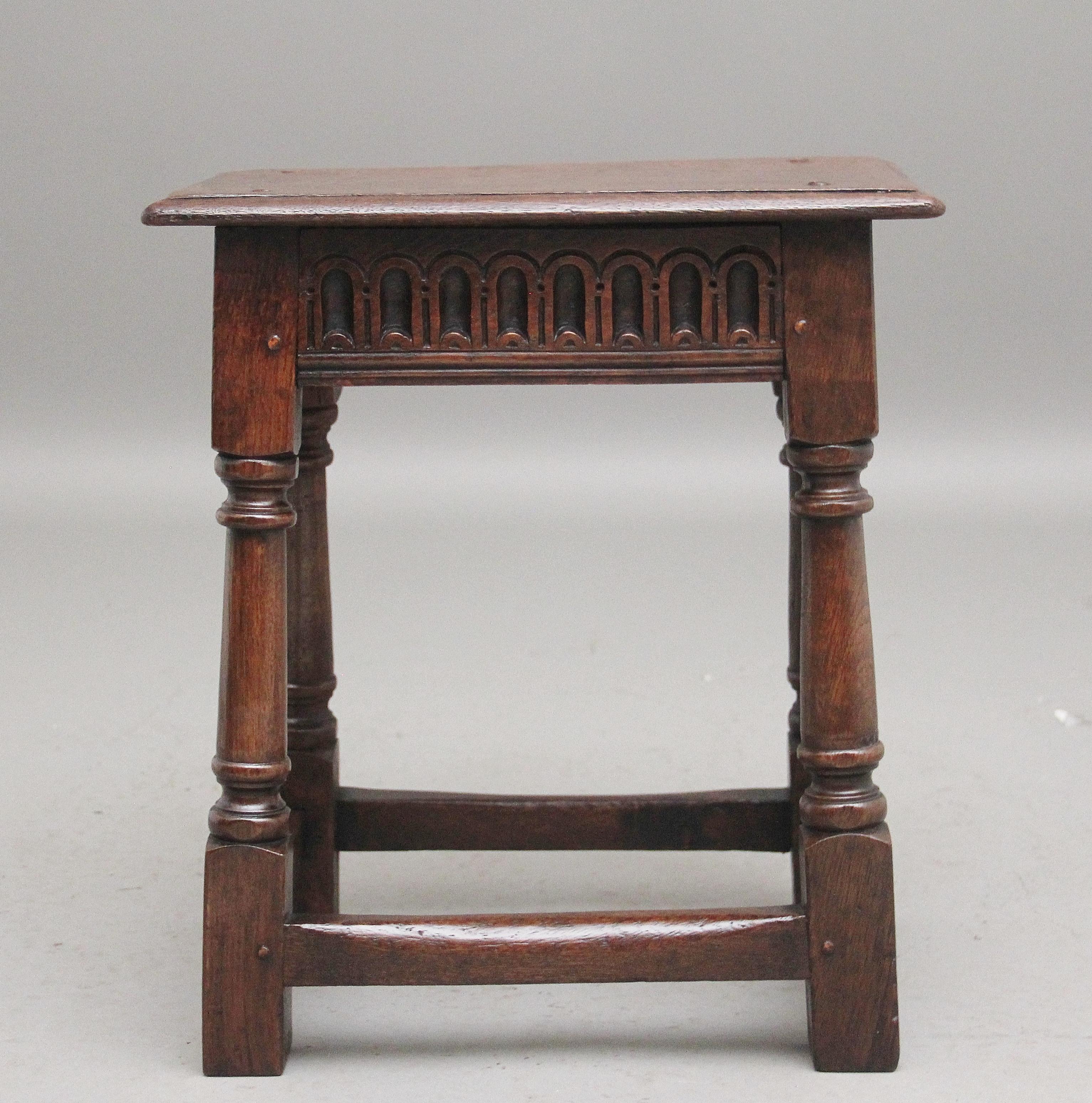 Early 20th Century oak joint stool in the 17th Century style, the moulded edge rectangular top with a decorative carved frieze below, raised on turned baluster supports united by stretchers and terminating on block feet.  Circa 1920.