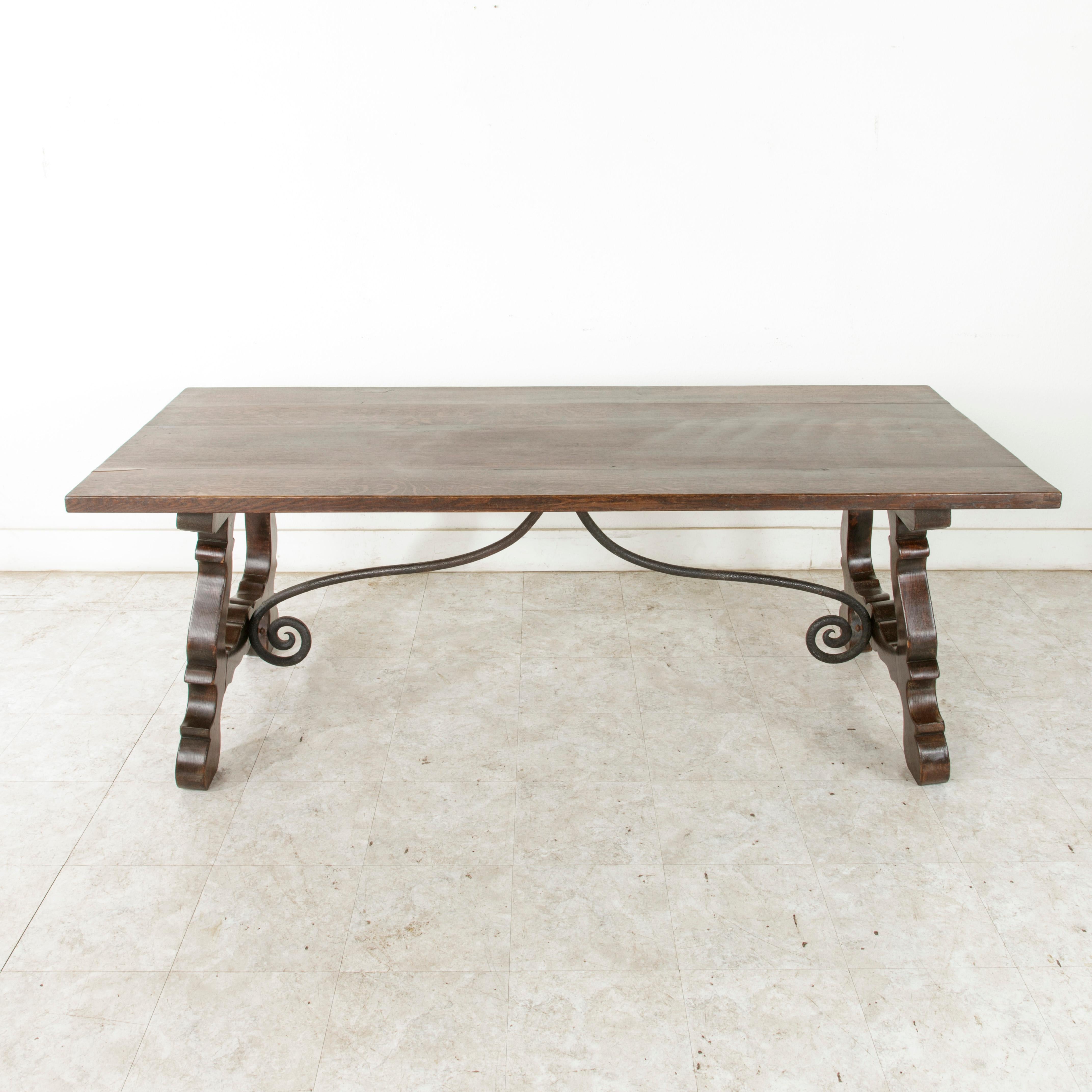 This beautifully carved Spanish Renaissance style dining table features a hand-forged wrought iron trestle. Its thick solid oak construction and dark patina give it a handsome old world feel, while its carved legs and slender trestle allow it to
