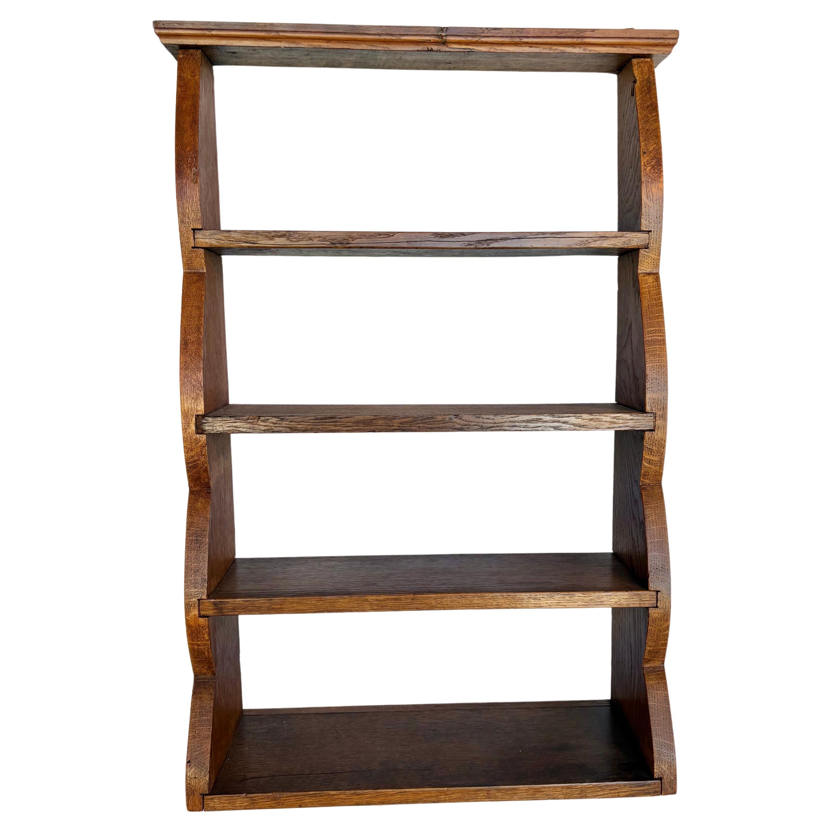 This Early 20th Century Wall Shelf was handcrafted from old growth oak in the early 1900's. The piece features gracefully curved risers that harmonizes rustic charm with a traditional feel. Each of the four shelves graduate in size beginning with