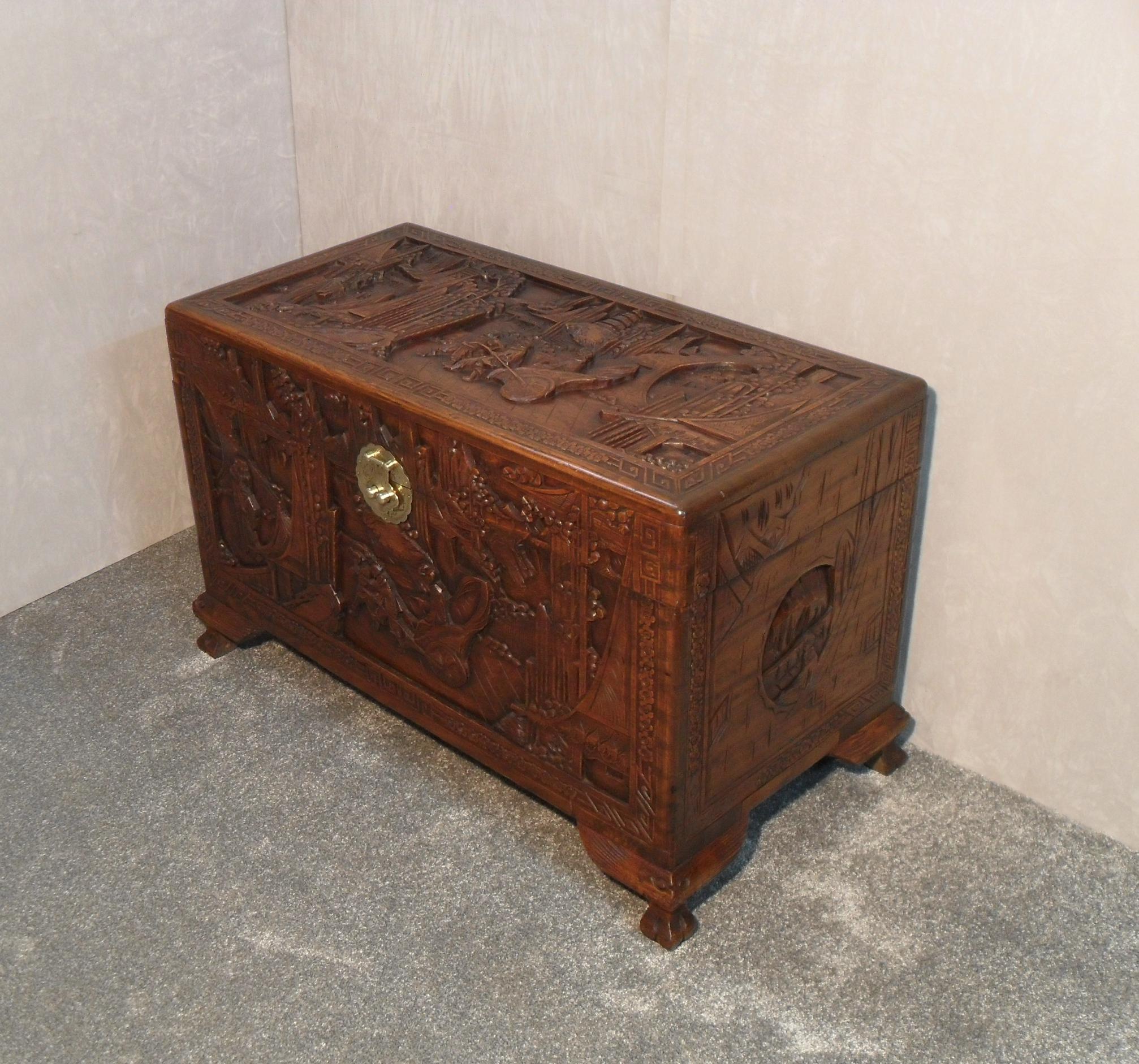 A very good quality and ornately carved freestanding Oriental camphor wood chest with carved scenes of a rickshaw cart, surrounded by trees and pagodas with a floral border. The chest retains its original engraved brass back plate and comes with a