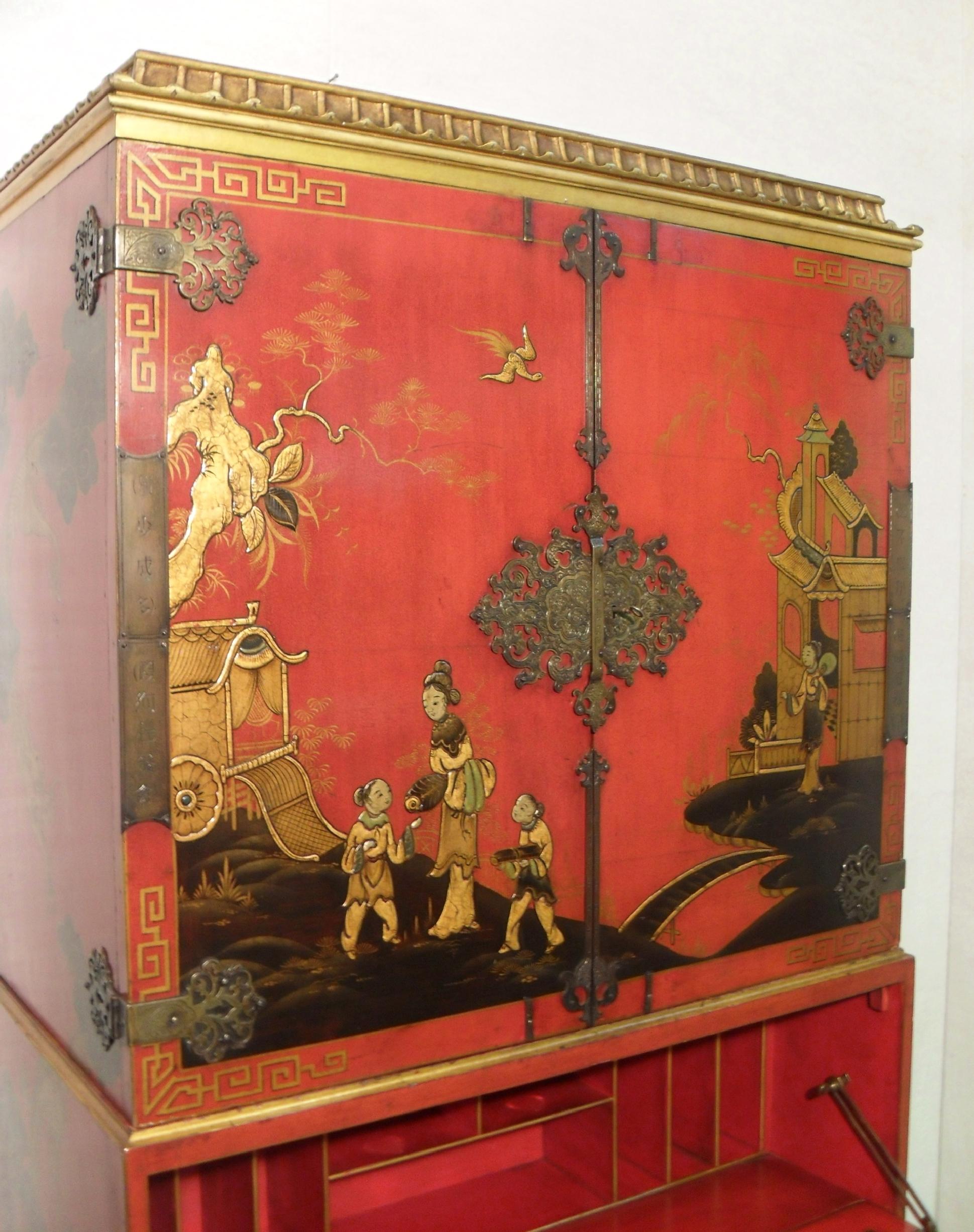 A decorative Oriental red chinoiserie writing cabinet on stand with beautifully hand painted gilt scenes in relief with dragons to the sides and pagoda top terminating to ball and claw feet.