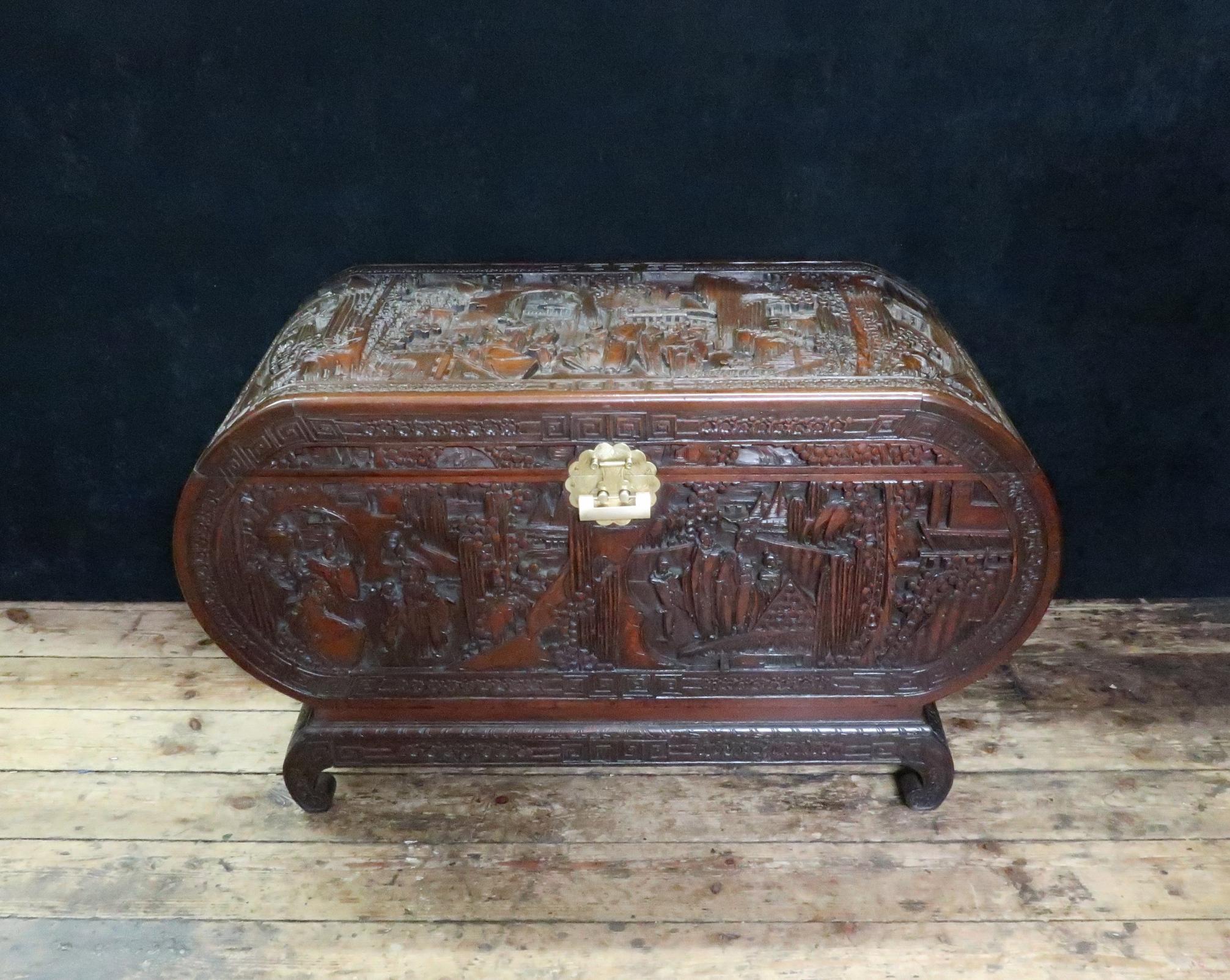 A superb oval shaped oriental freestanding teak chest profusely and deeply carved with scenes of trees, flowers, mountains, people and pagodas within a floral border with kang table style base on scrolling legs. The chest retains its original