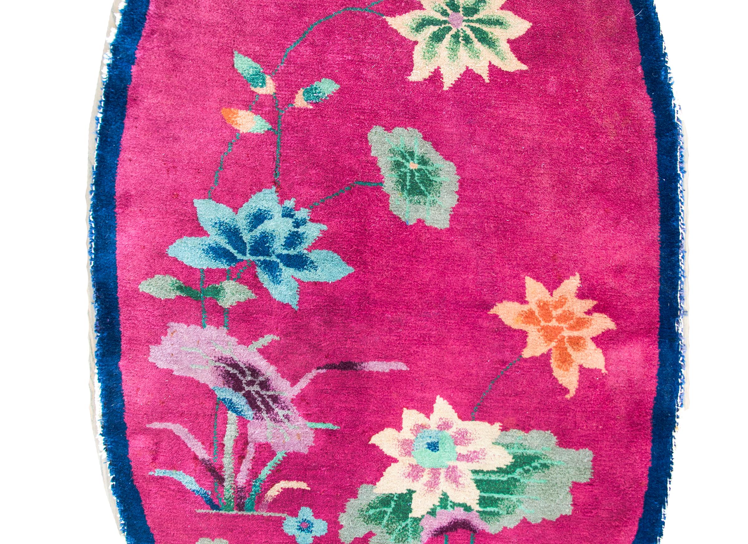 A rare early 20th century oval Art Deco rug with a thin indigo border surrounding a fuchsia field covered in multi-colored lotus blossoms springing from a pond.