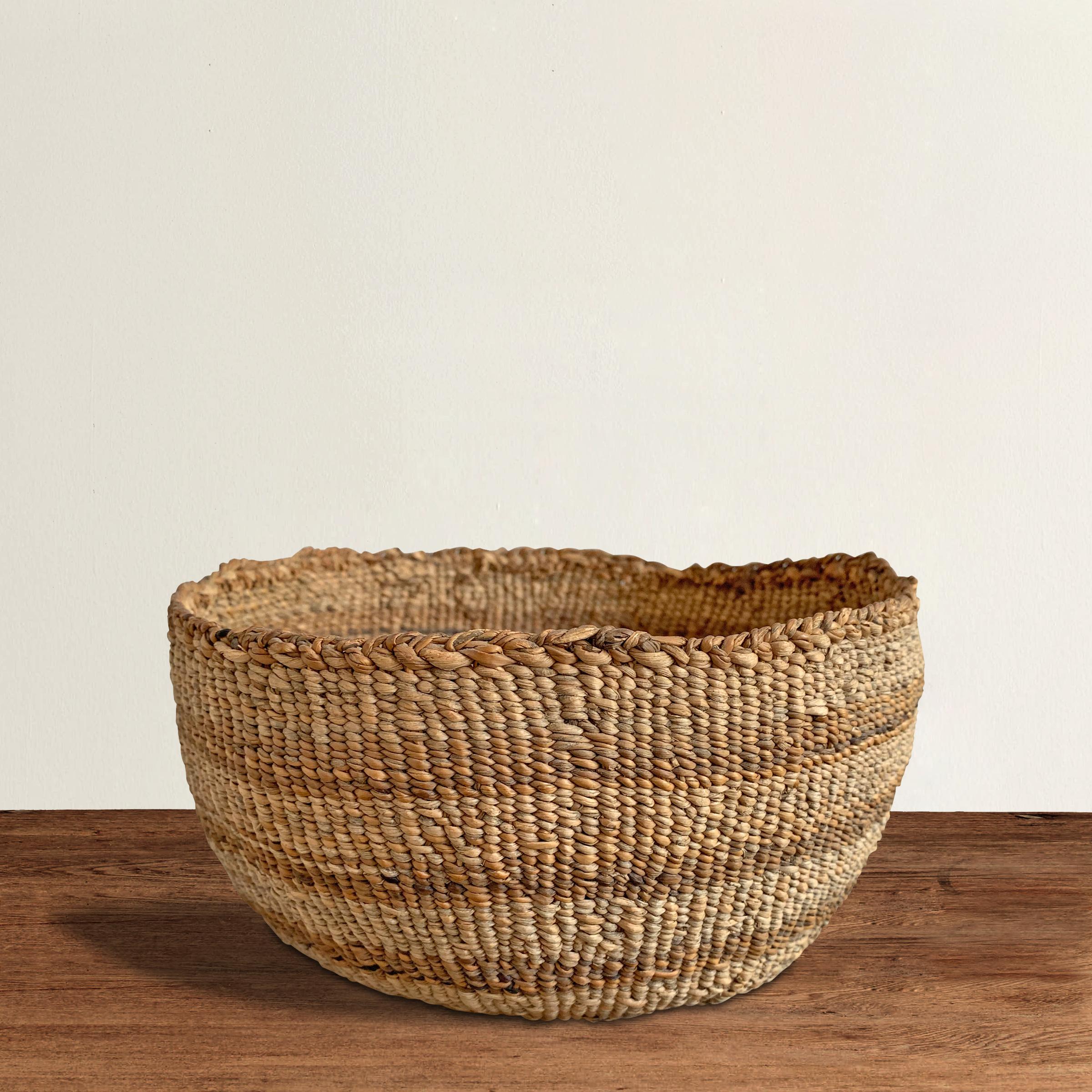 A wonderful and charming early 20th century Pacific NW Native American handwoven basket with a decorative linear pattern using varying shads of natural grasses.