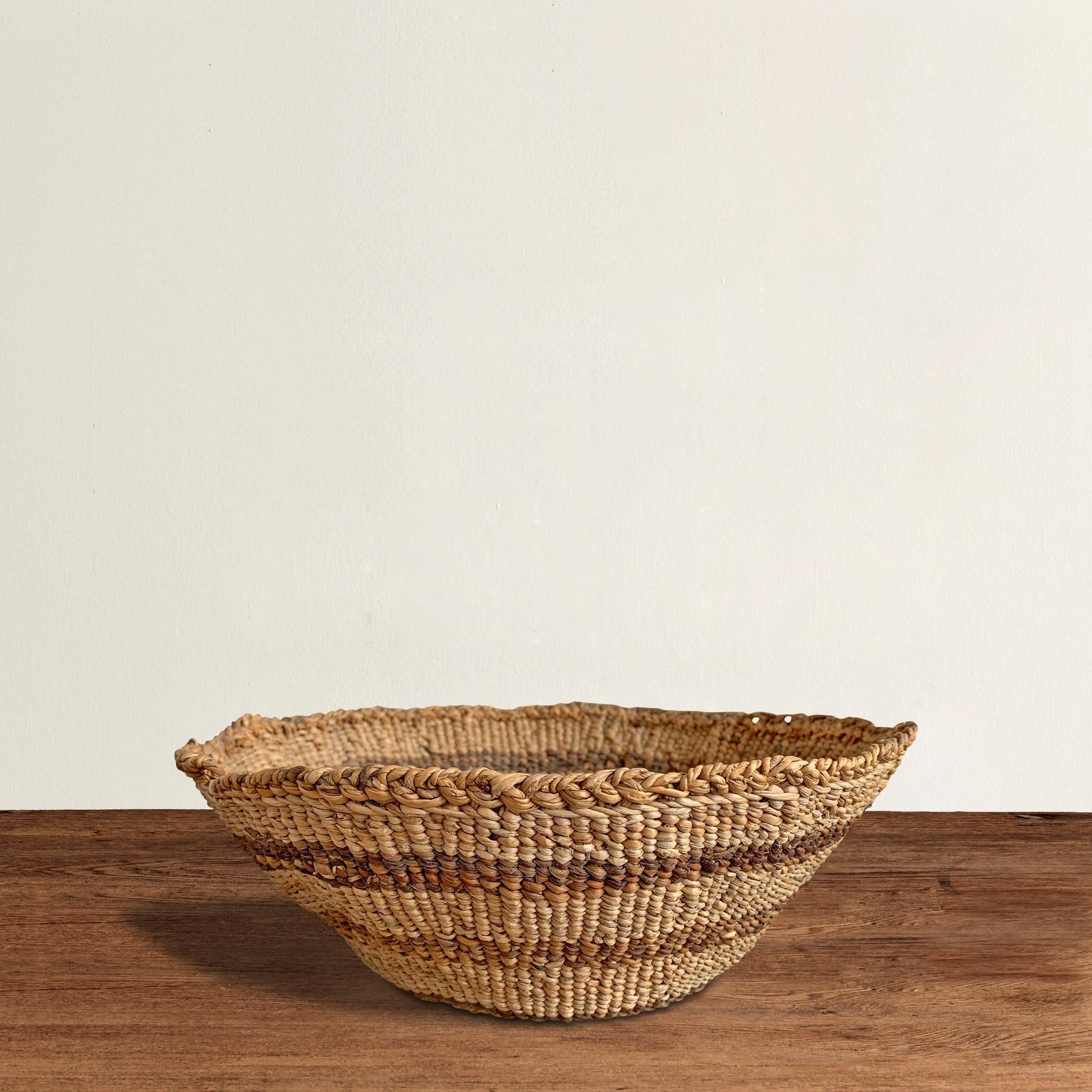 A wonderful and charming early 20th century Pacific NW Native American handwoven basket with a decorative linear pattern using varying shades of natural grasses.