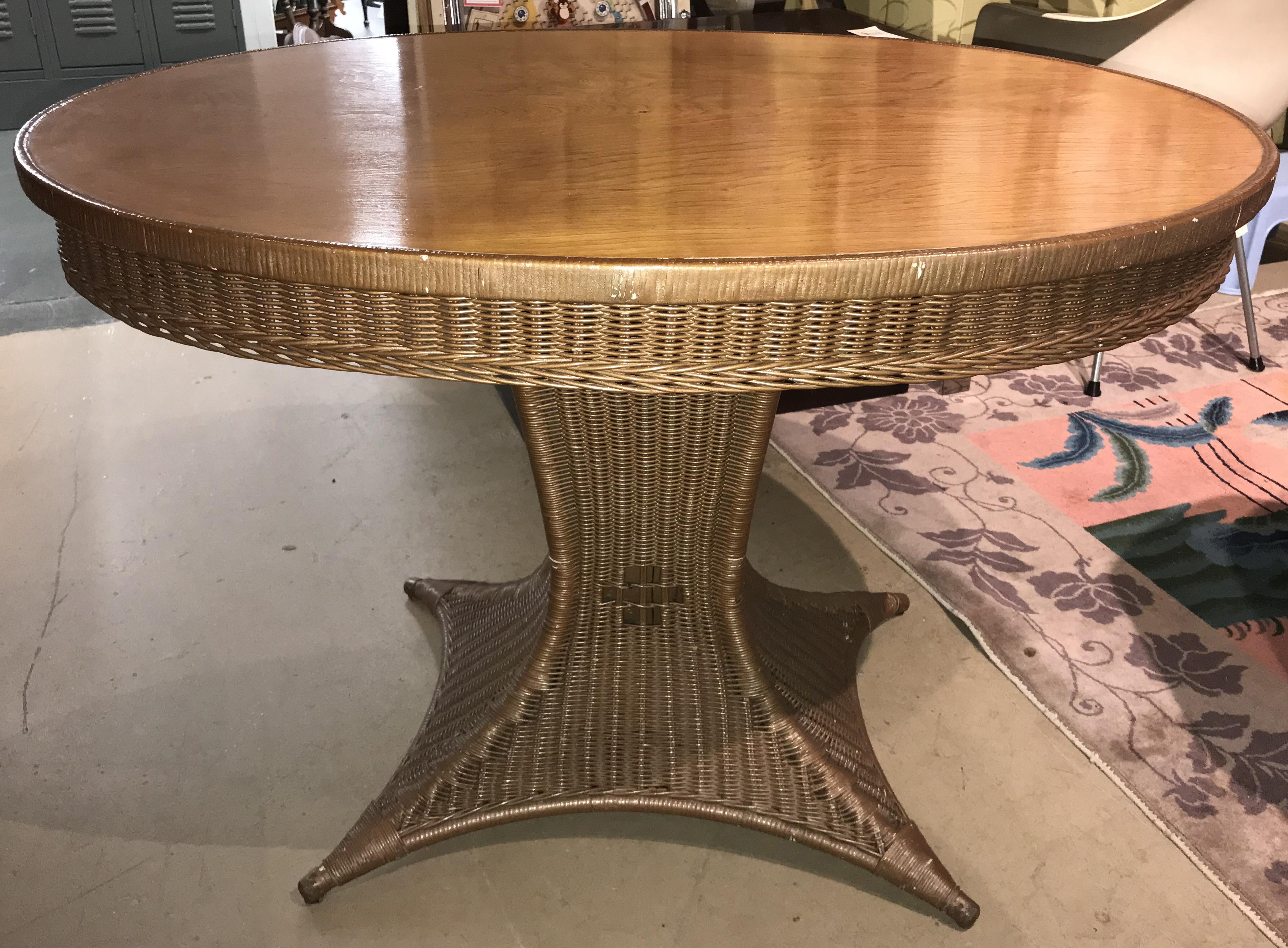 A fine oval wicker table with plank wood top on a square central tapering pedestal base which flares out to four supporting footed corners. A Paine Furniture Co, Boston MA metal tag is attached to the base. Paine Furniture Co was founded in Boston