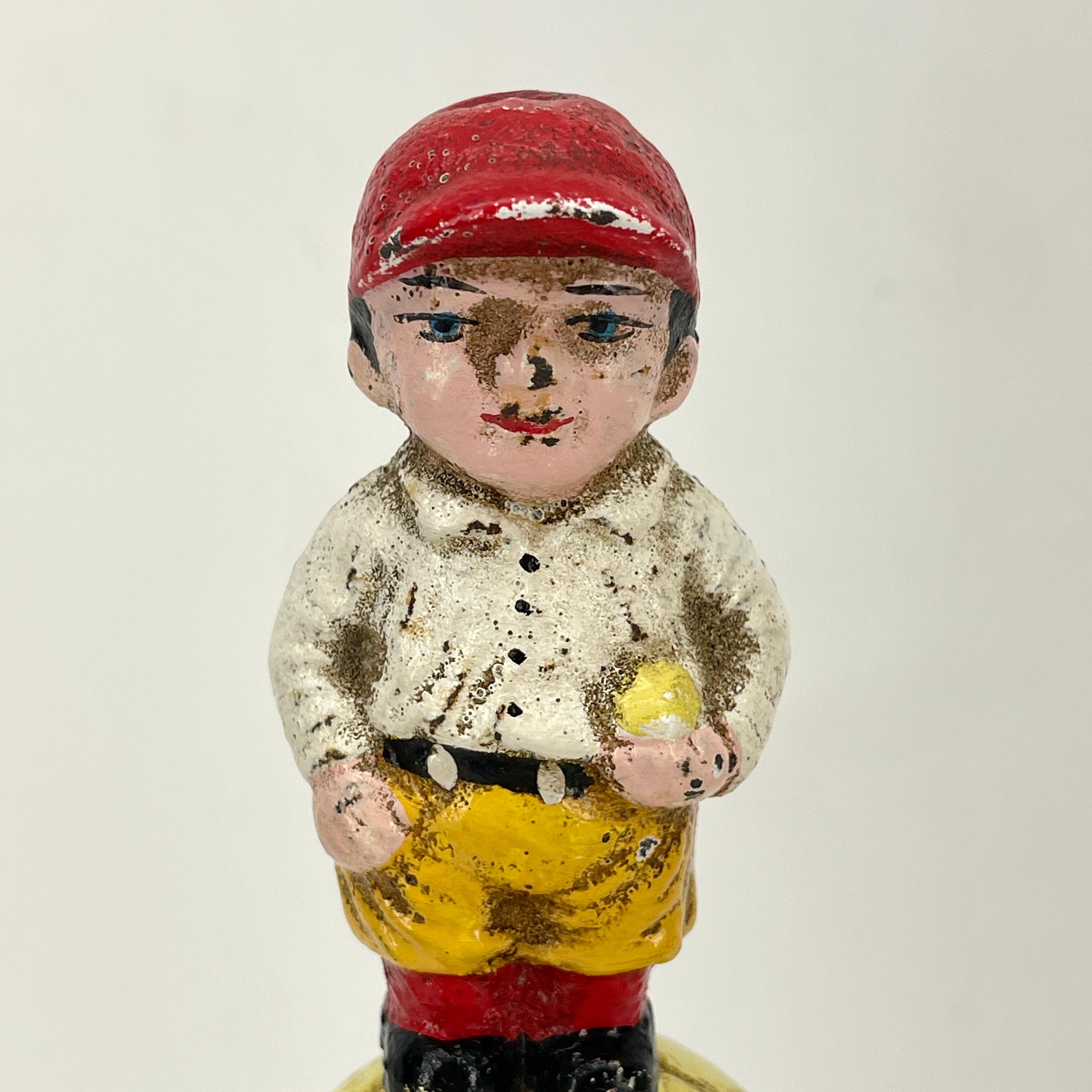 Small 19th century American cast iron piggy bank or money box. This sweet bank has a baseball player sitting atop his baseball in original antique painted patina. Mounted on small square lucite base. It is left intentionally in the distressed look