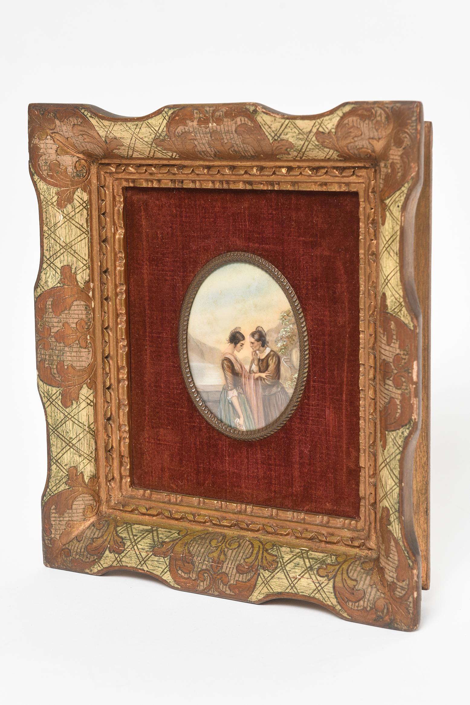 Early 20th century painting on celluloid of the women by the water having a deep conversation. It looks as if the older one is advising the younger one. The painting is set is a giltwood frame with a burgundy velvet background.