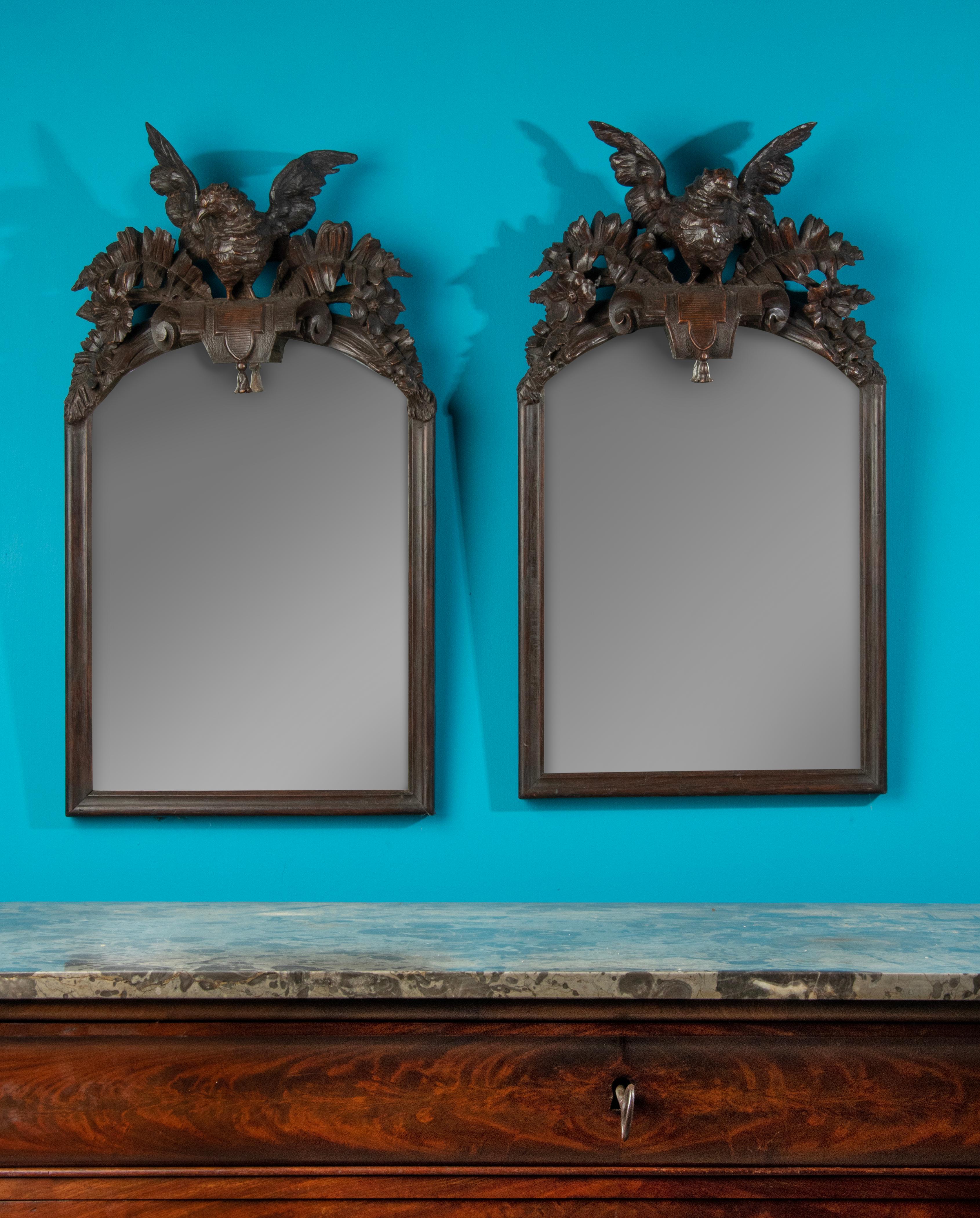 A pair of elegant French mirrors, carved from solid oakwood in Black Forest style. Bird is depicted on both mirrors, each in an asymmetrical manner, so that it is an original couple. The birds are flanked by flowers and leaves ornaments. These