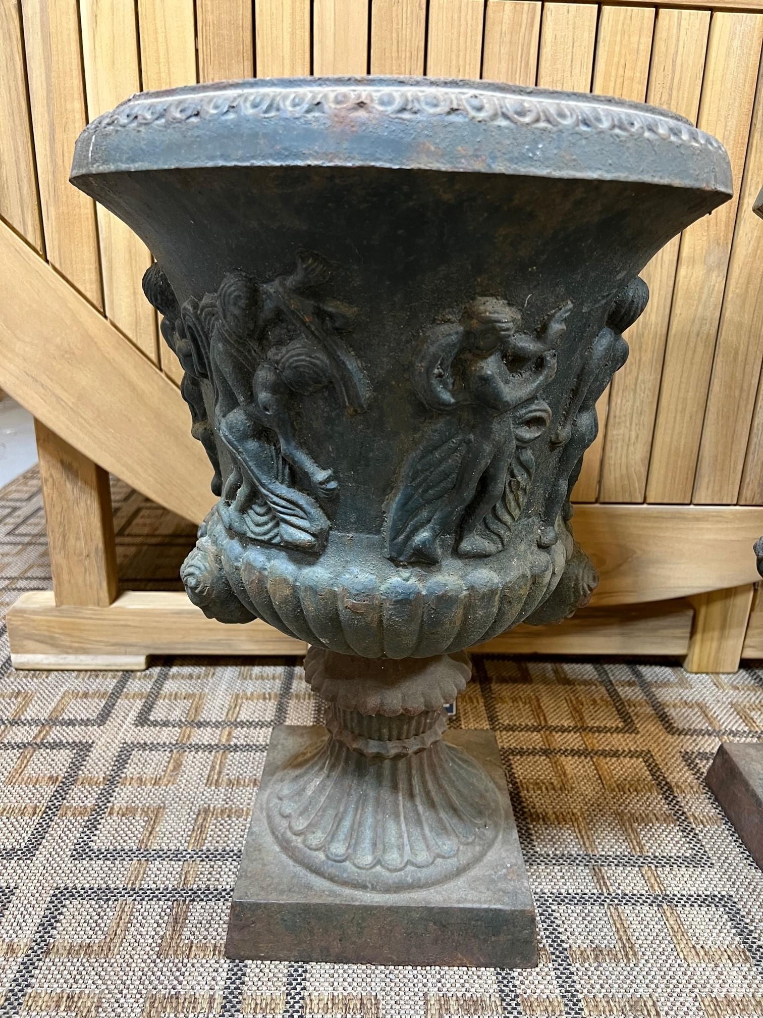 Magnificent pair of neoclassical revival cast iron garden urns. The urns are decorated with Greco-Roman figures with a fluted column base. A beautiful pair of cast iron figural urns from an estate in Greenwich Ct. They are a nice size for any garden