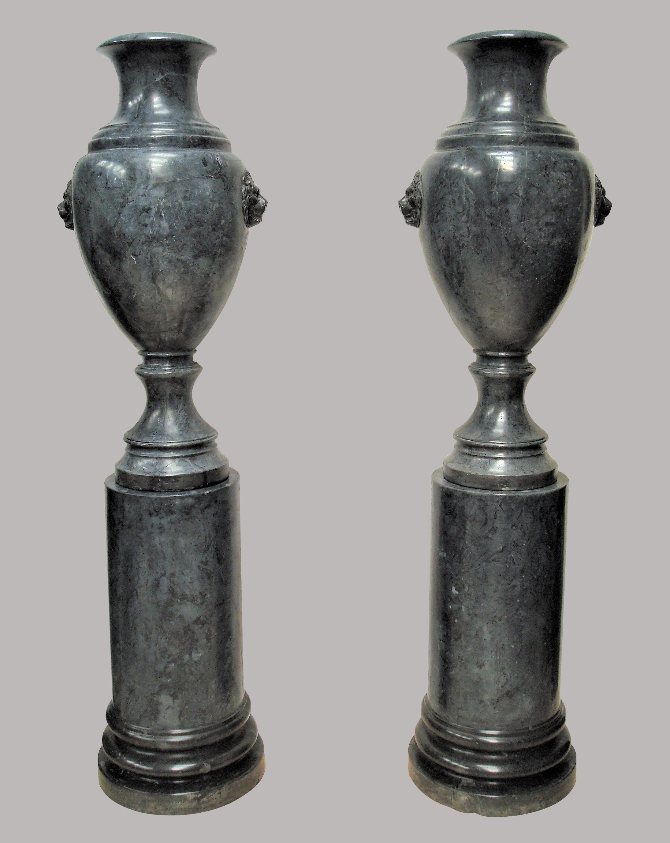An imposing early 20th century pair of Scagliola urns on pedestals of monumental proportions, of steel blue color. The neoclassical style urns of Amphora shape with large black lion masks to either side. Standing on circular column pedestals with