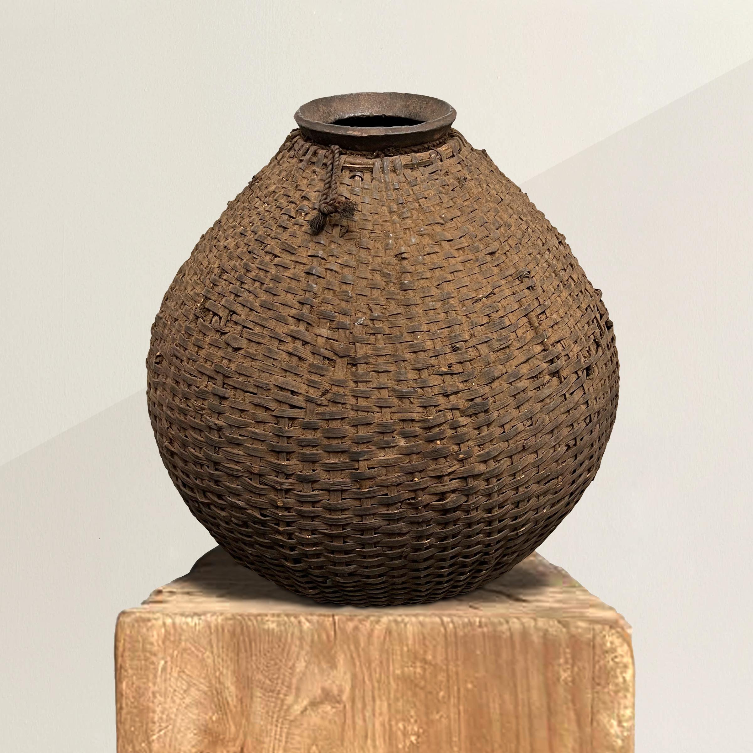 An incredible early 20th century Makenge hand-built ceramic palm wine pot with a graceful shape including a narrow neck and a wide belly. The pot is covered in a hand-woven wicker basket covering, skillfully woven to form perfectly to the shape of