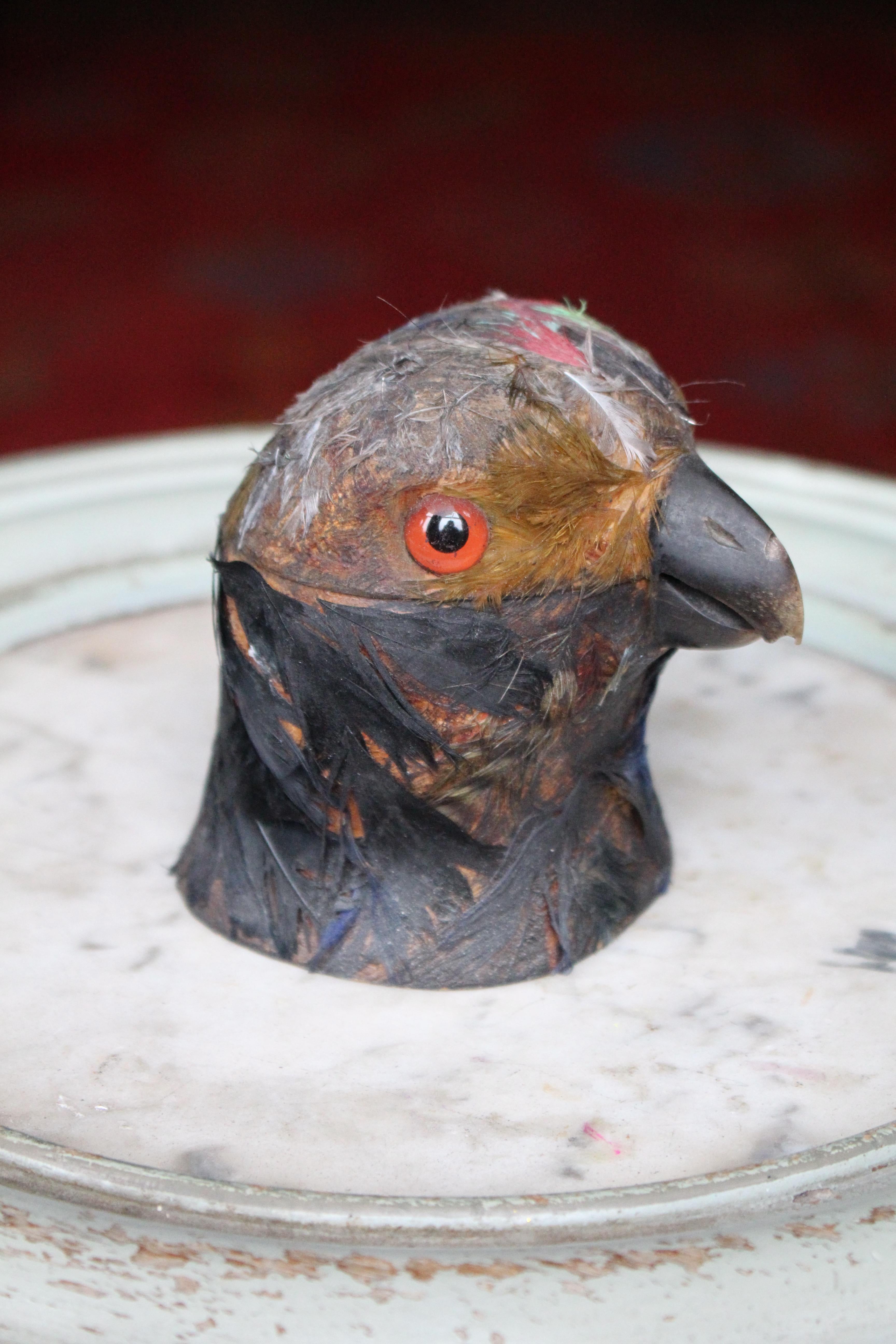 A quirky little ink well in the form of a parrot/parakeet, turned wooden caucus with applied beak, glass eyes and hand dyed feathers. 

The top section hinged to reveal the inkwell with its original glass liner, plenty of ink stains to the wooden