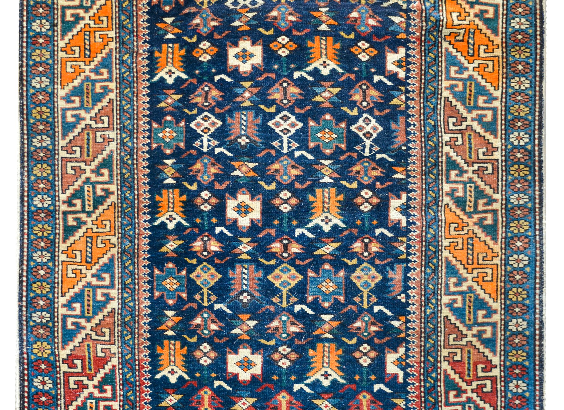 A early 20th century Persian Perepedil rug with a beautiful all-over field of stylized flowers woven in crimson, orange, white, and gold against a dark indigo background and surrounded by wonderful geometric patterned border woven in similar colors