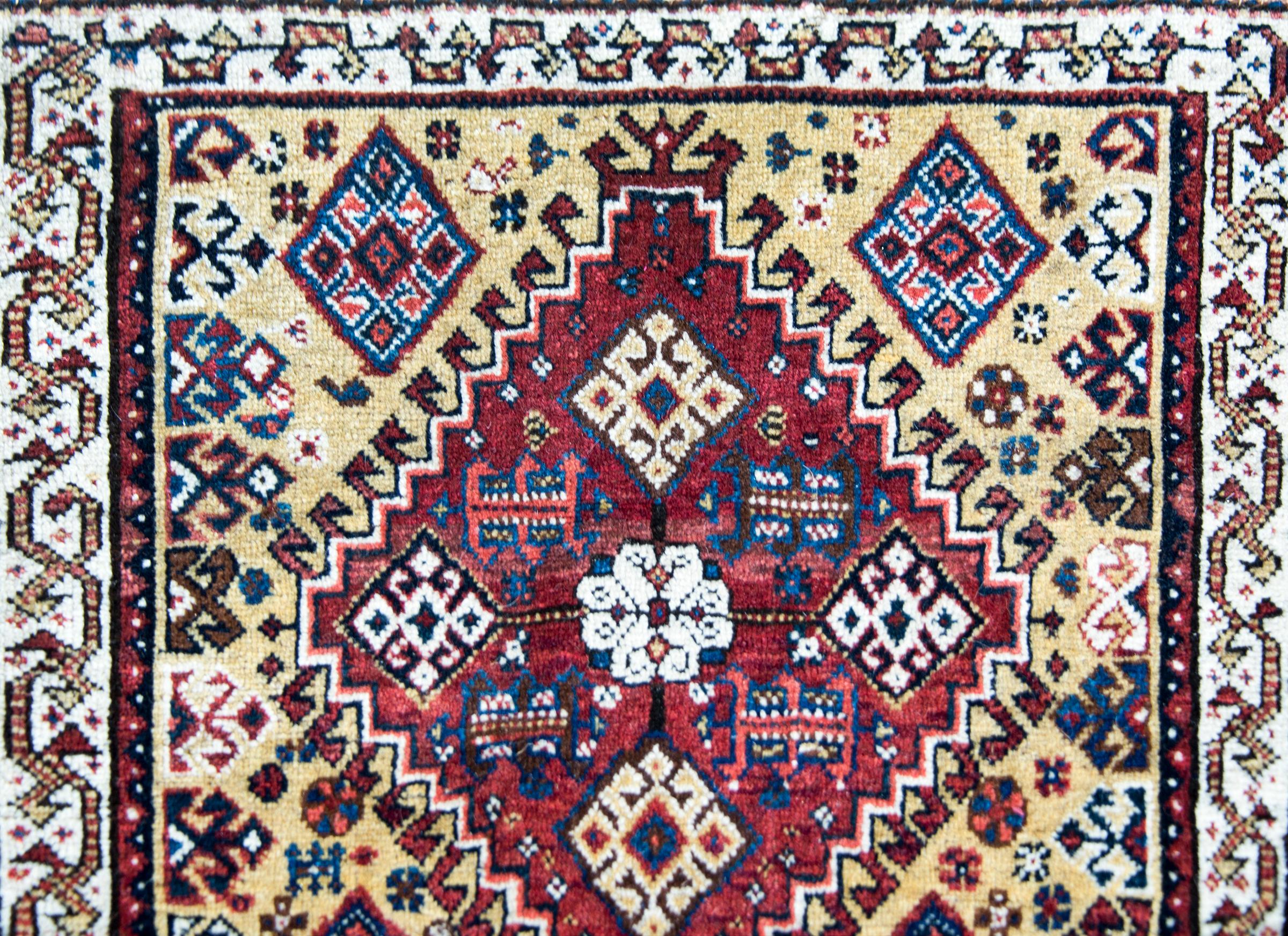 A beautiful early 20th century Persian Afshar rug with a large central central diamond pattern with stylized flowers woven in crimson, white, indigo, and yellow, and surrounded by a border with stylized scrolling vine patterns.