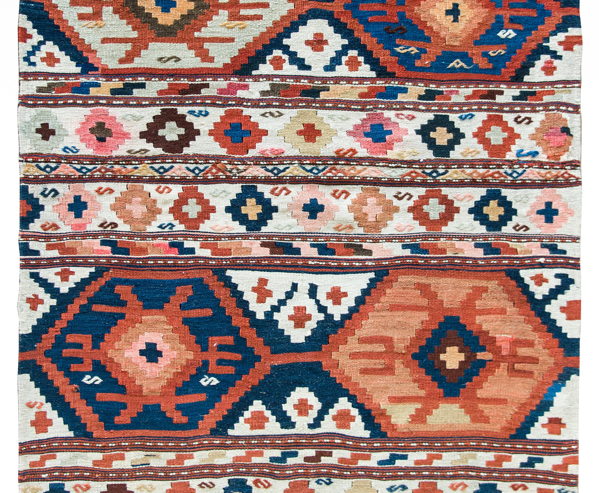A beautiful early 20th century Persian Azari Kilim rug with four large geometric stylized flowers amidst a field of more stylized flowers arranged into stripes across the field, and solid colored stripes at each end.