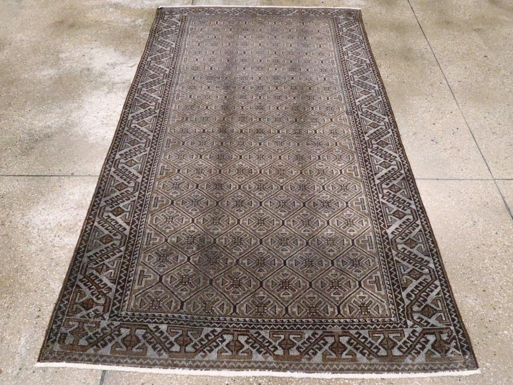 Un tappeto d'accento persiano Baluch vintage. Un reticolo esagonale molto ravvicinato che racchiude quatrefogli floreali geometrici nei toni del carbone, del grigio-blu e del marrone è incorniciato da un bordo grigio-blu con barre uncinate oblique e