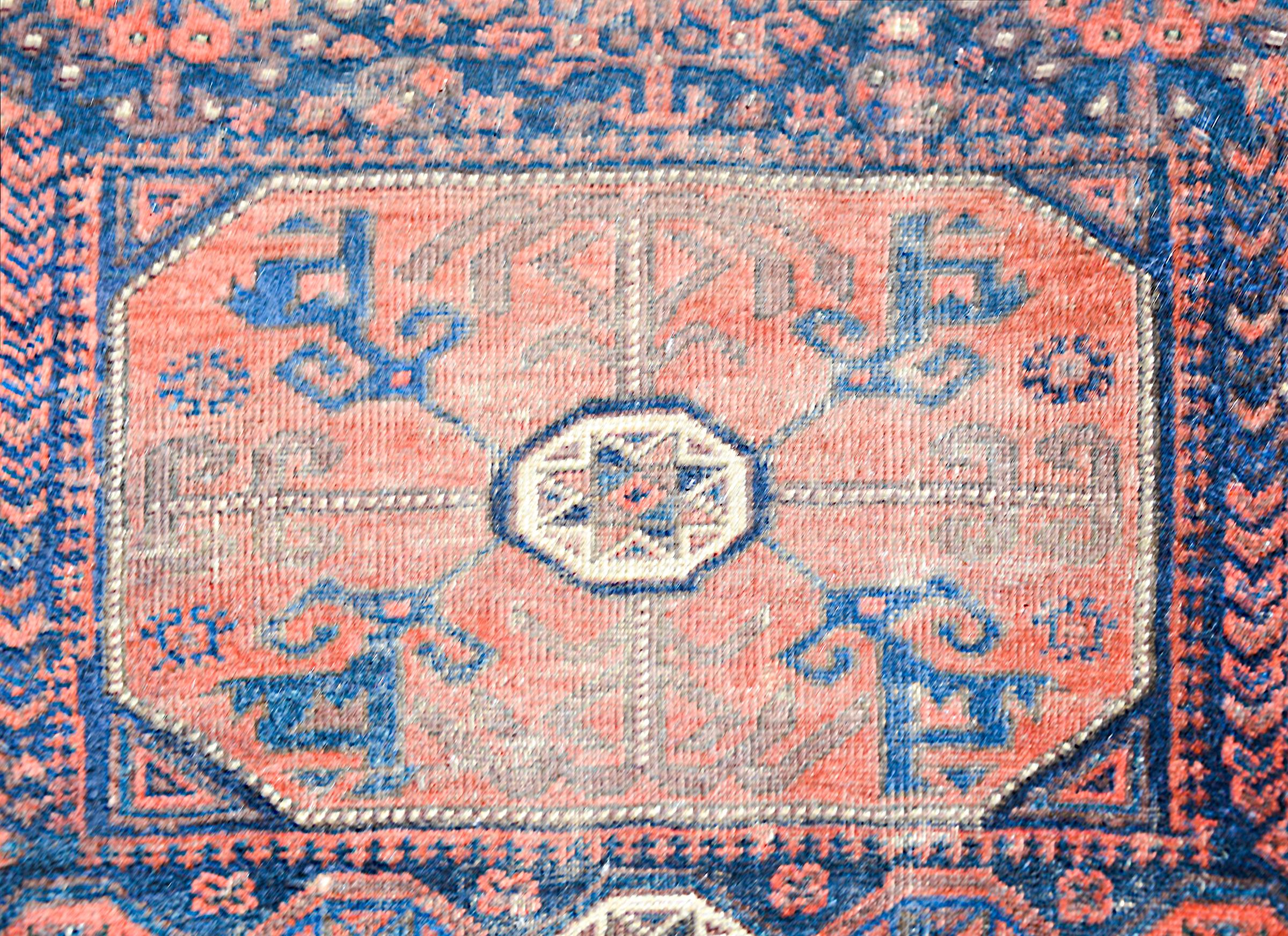 Magnifique tapis persan Baluch du début du XXe siècle, présentant un fantastique motif tribal contenant de multiples fleurs stylisées tissées en cramoisi, indigo, brun et blanc, et entouré d'une bordure à motifs de fleurs et de feuilles