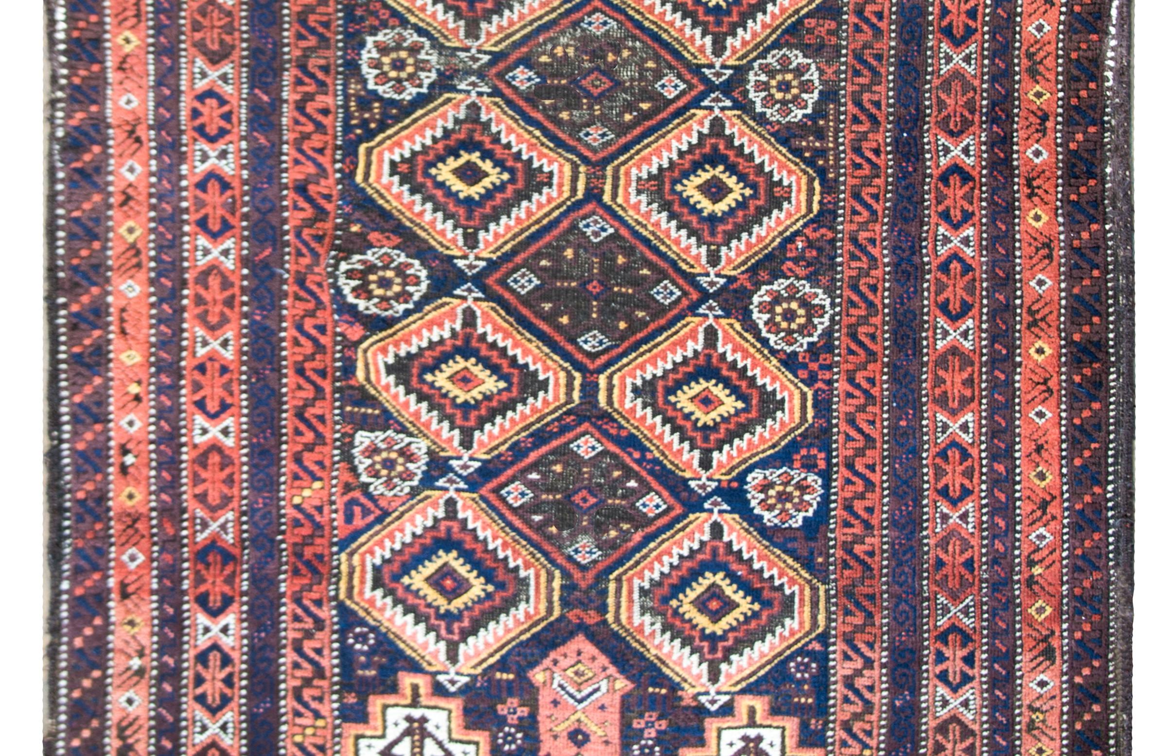 A stunning early 20th century Persian Baluch rug with an all-over diamond pattern woven with petite stylized flowers, all woven in orange, gold, white, and indigo wool, set against a brown background, and surrounded by a complex border of multiple