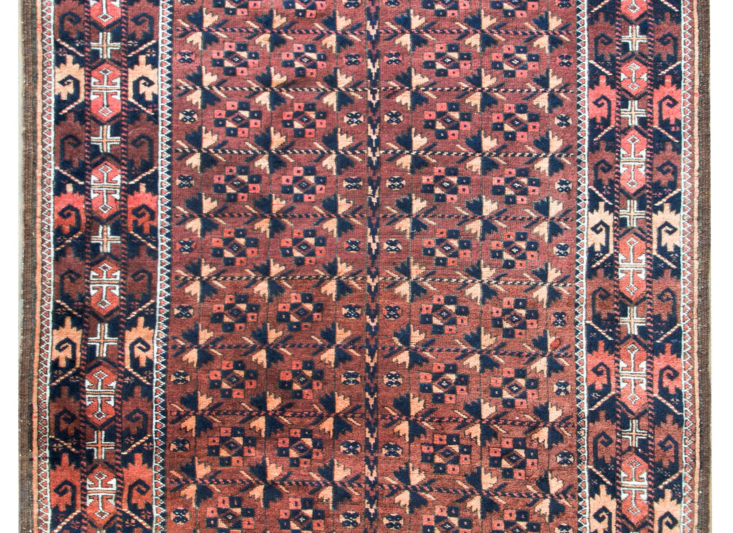 A beautiful early 20th century Persian Baluch rug with an all-over stylized flower pattern woven in red, orange, and black wool, set against a brown background.  The border is wonderful with even more stylized flowers and leaves woven in similar