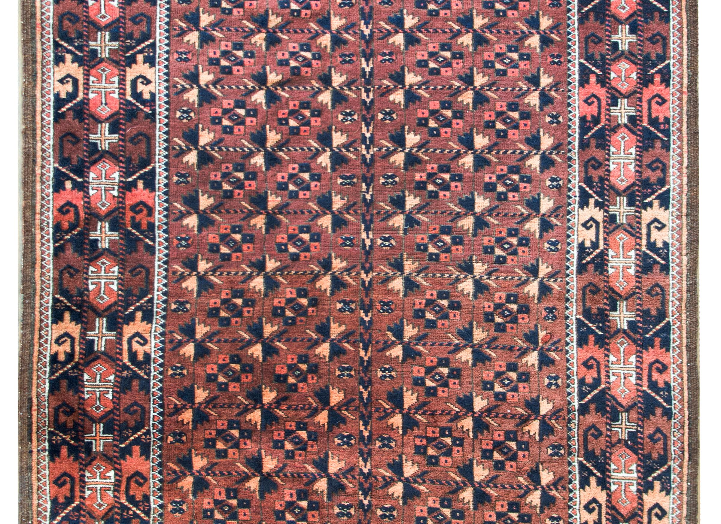 Un bellissimo tappeto persiano Baluch dell'inizio del XX secolo con un motivo floreale stilizzato all-over in lana rossa, arancione e nera, su uno sfondo marrone.  Il bordo è meraviglioso con fiori e foglie ancora più stilizzati e tessuti in colori