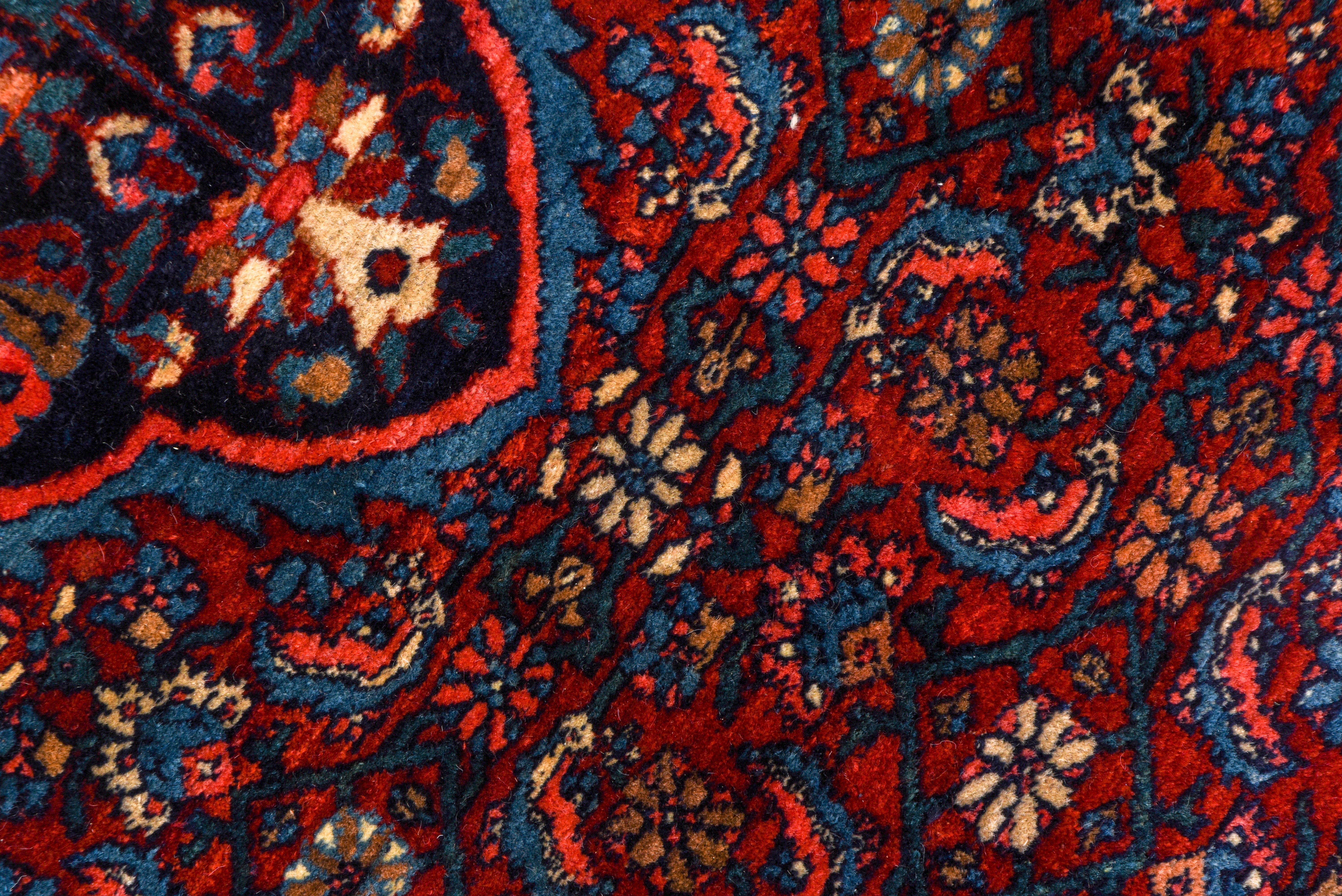 This west Persian Kurdish town carpet has an all Herati field pattern: the red ground and the pendanted navy medallion and the triangular navy corners all share a Classic small rosette, leaf and open diamond pattern. The precisely rendered navy