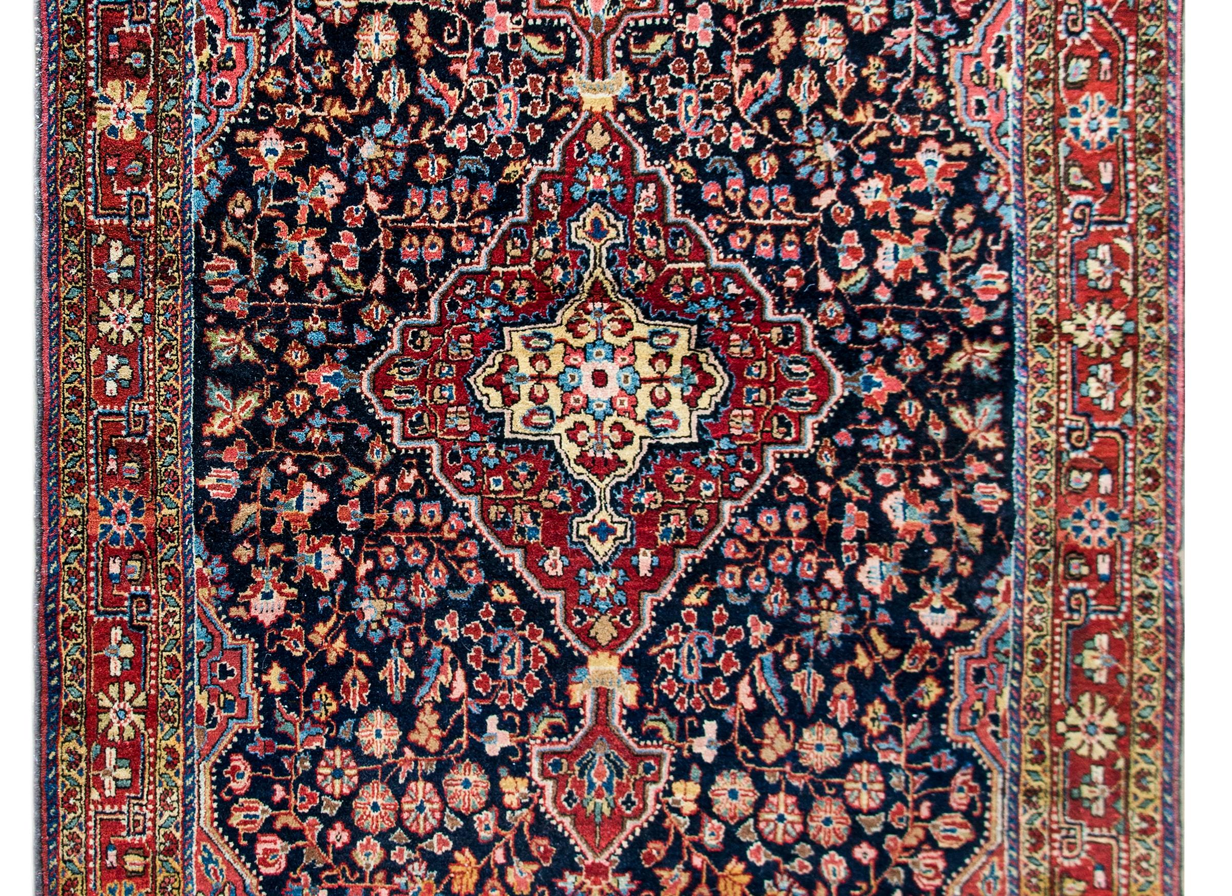 An early 20th century Persian Bidjar rug with a wonderful floral medallion living amidst a field of densely woven flowers and scrolling vines, and surrounded by a wide floral border composed of multiple thin stripes, and all woven in cranberry,