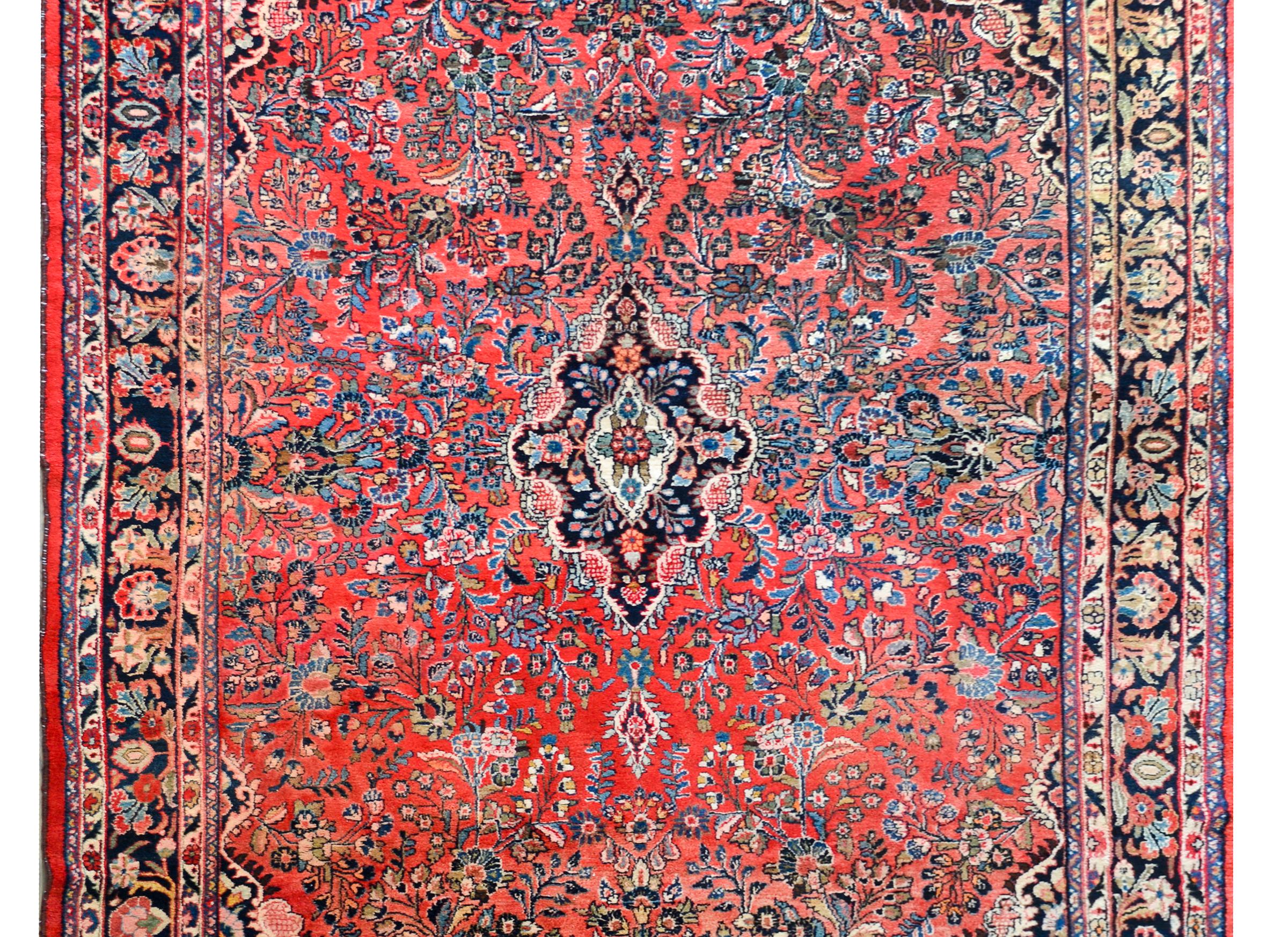 A beautiful early 20th century Persian Dargazin rug with a large central medallion against a dark indigo background floating amidst a field of myriad floral clusters woven in light and dark indigo, cream, and pink, and set against a gorgeous abrash