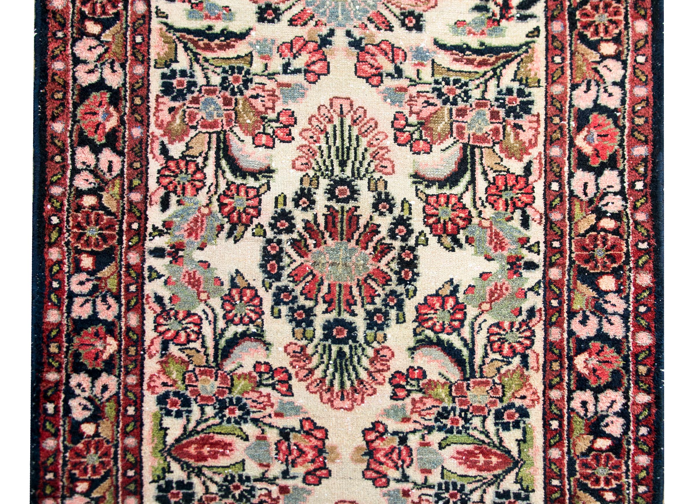 A stunning early 20th century Persian Dargazin runner with a mirrored all-over floral pattern with myriad flowers and leaves, surrounded by a complex border with repeated flowers and vines, and woven in cranberry, pink, blush, green, and dark indigo