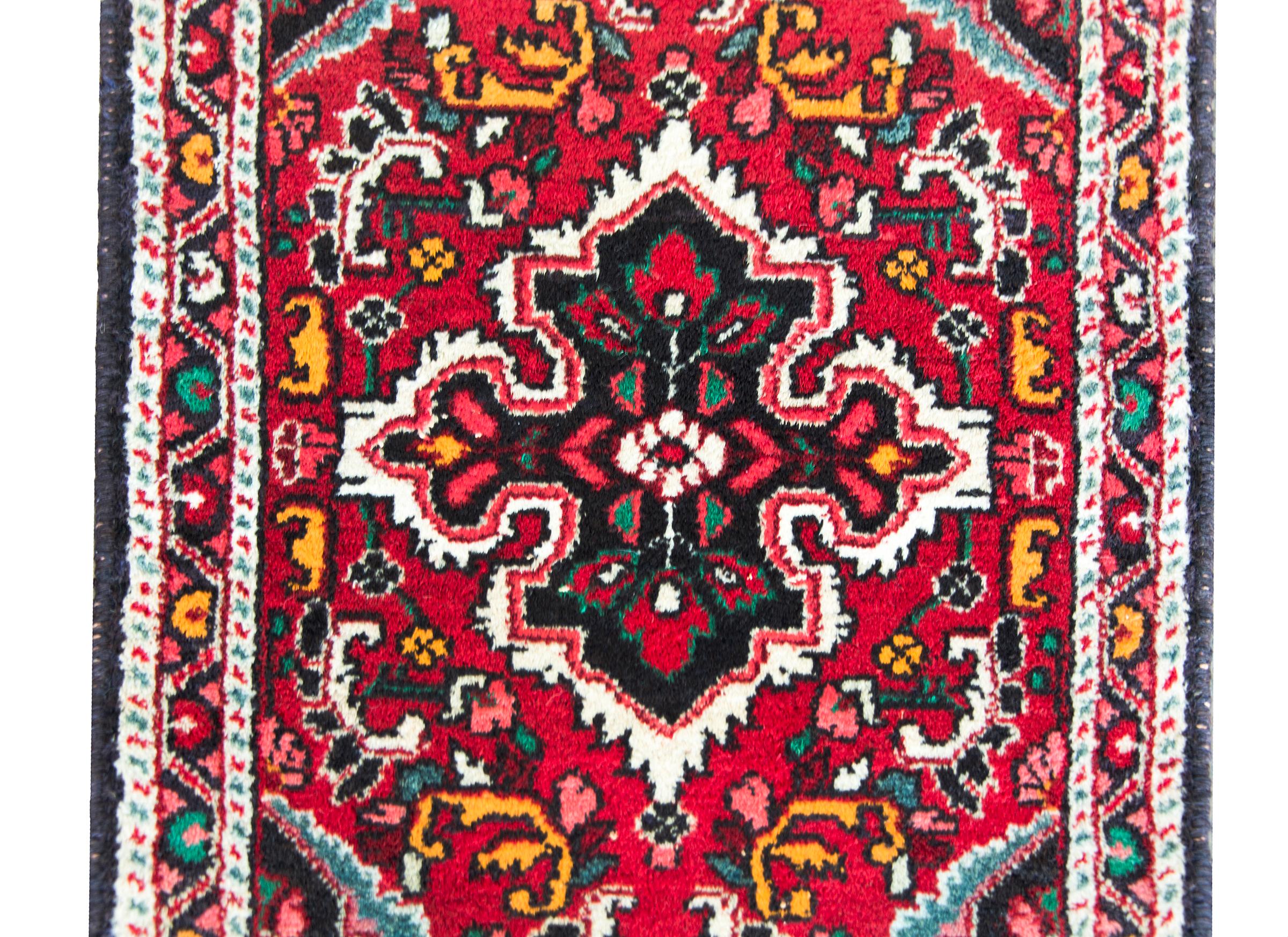 An early 20th century Persian Hamadan rug with a central floral medallion amidst a field of scrolling vines and flowers, al woven in pink, green, orange, crimson, and white, and surrounded by several petite floral patterned stripes.