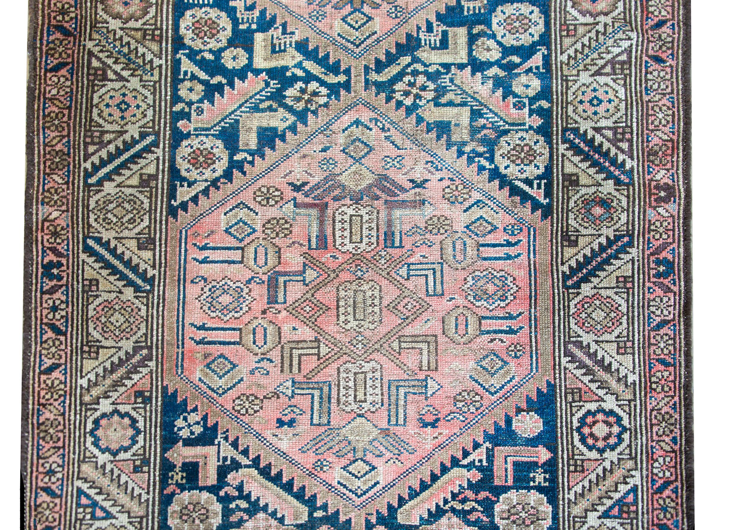 A beautiful early 20th century Persian Hamadan rug with two large medallions with stylized leaves and flowers woven in muted reds, indigos, browns, and creams, set against an indigo field with more stylized flowers and chickens. The border is wide