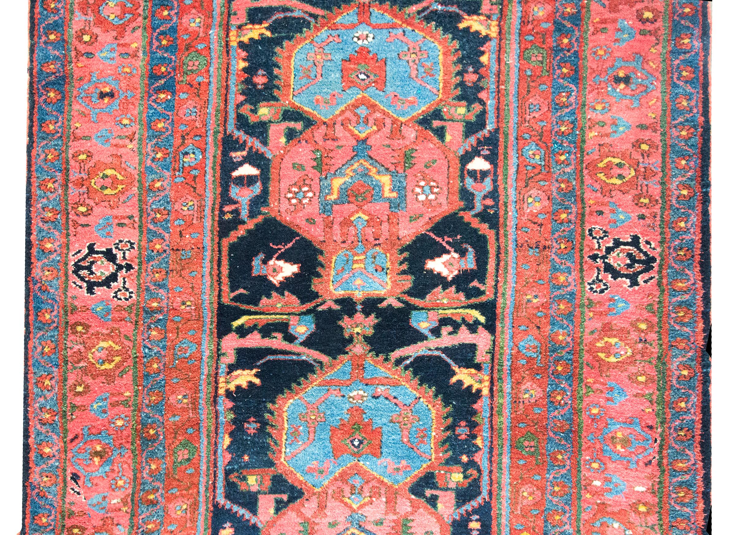 Woven in the early 20th century in western Iran, this Persian Hamadan rug features a striking central medallion filled with stylized flowers and scrolling vines, all rendered in rich shades of dark and light indigo, salmon, yellow, brown, and green